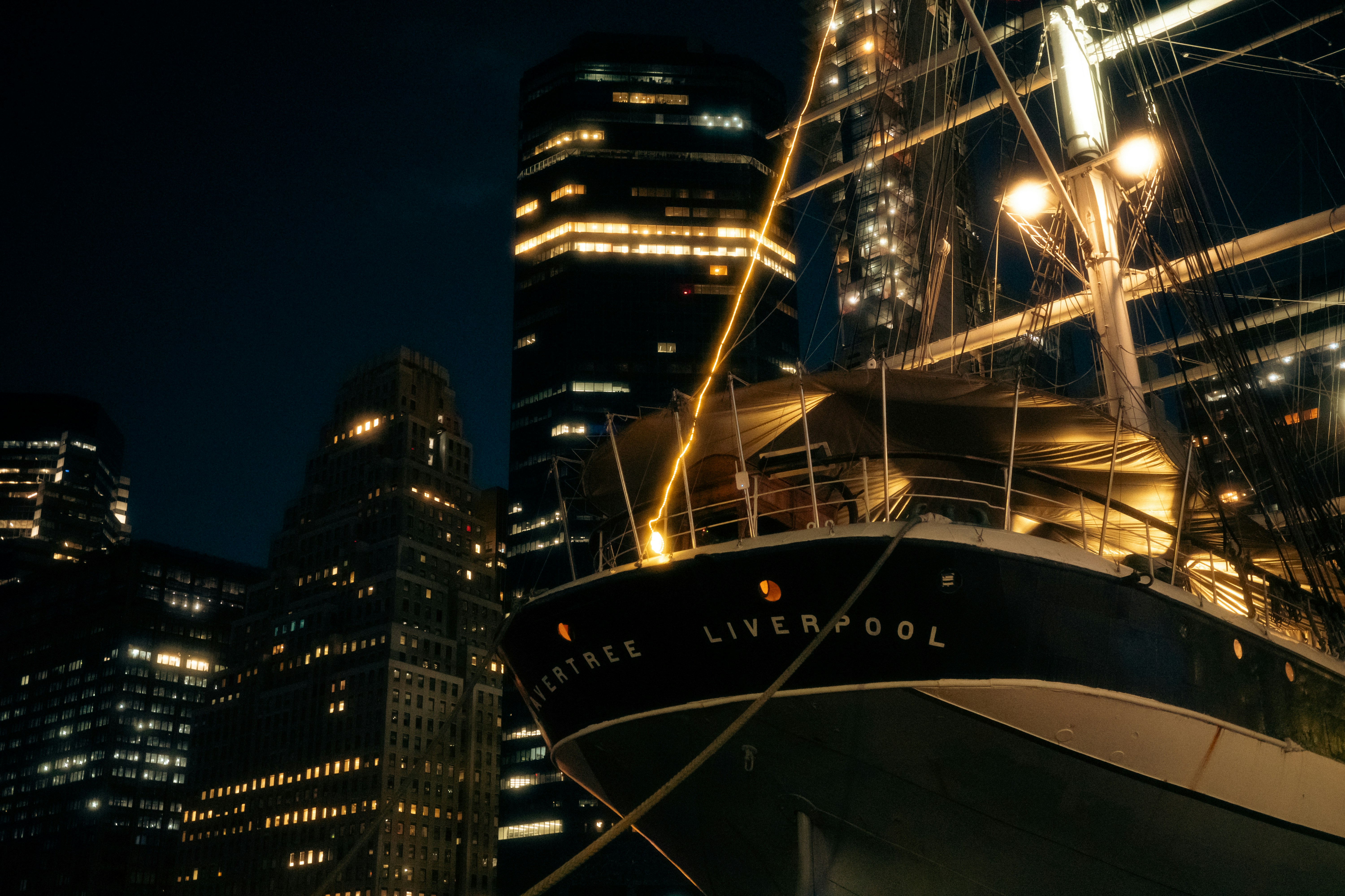 The Wavertree ship docked at night with illuminated skyscrapers in the background