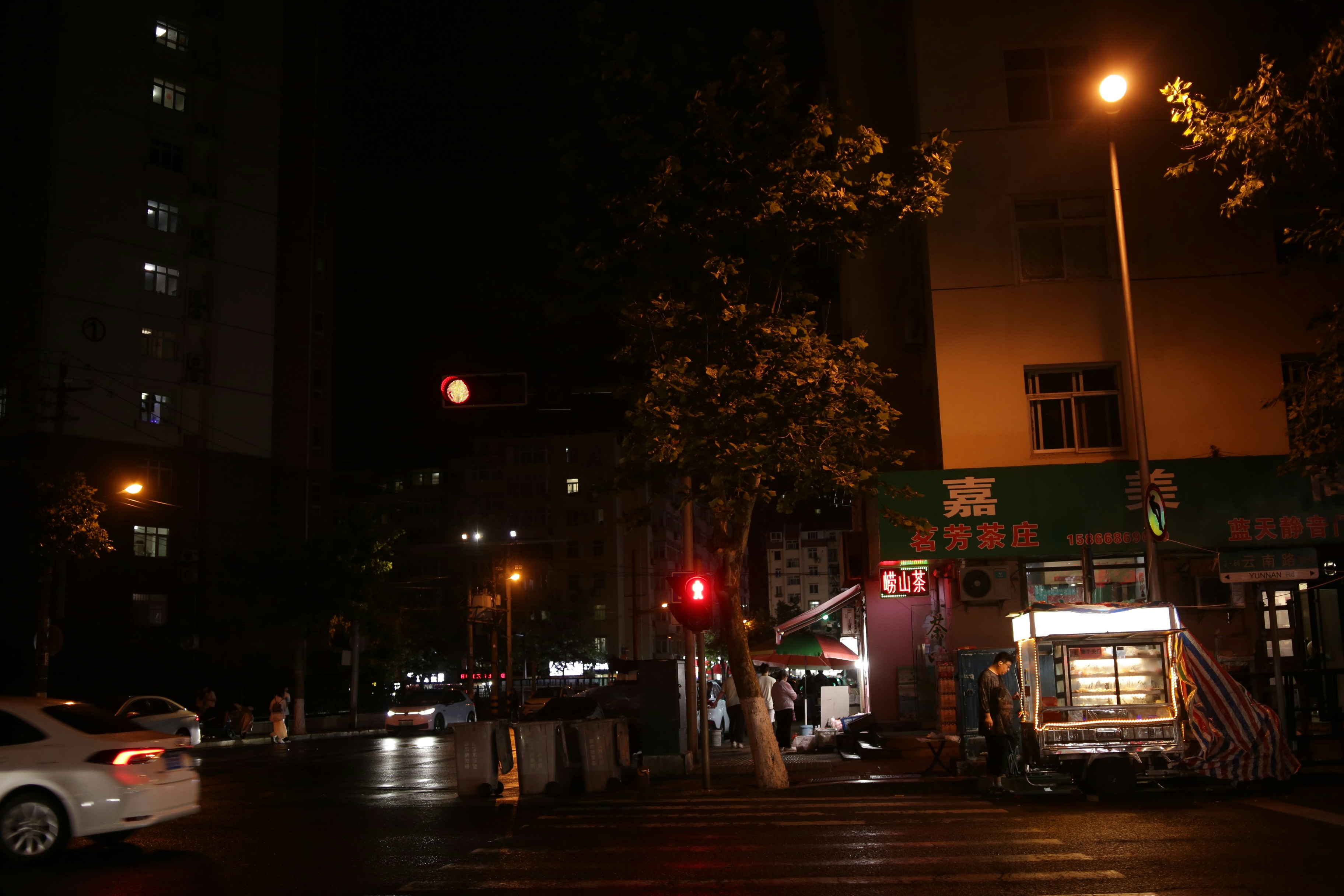 A street food cart on a dark city street at night with traffic lights