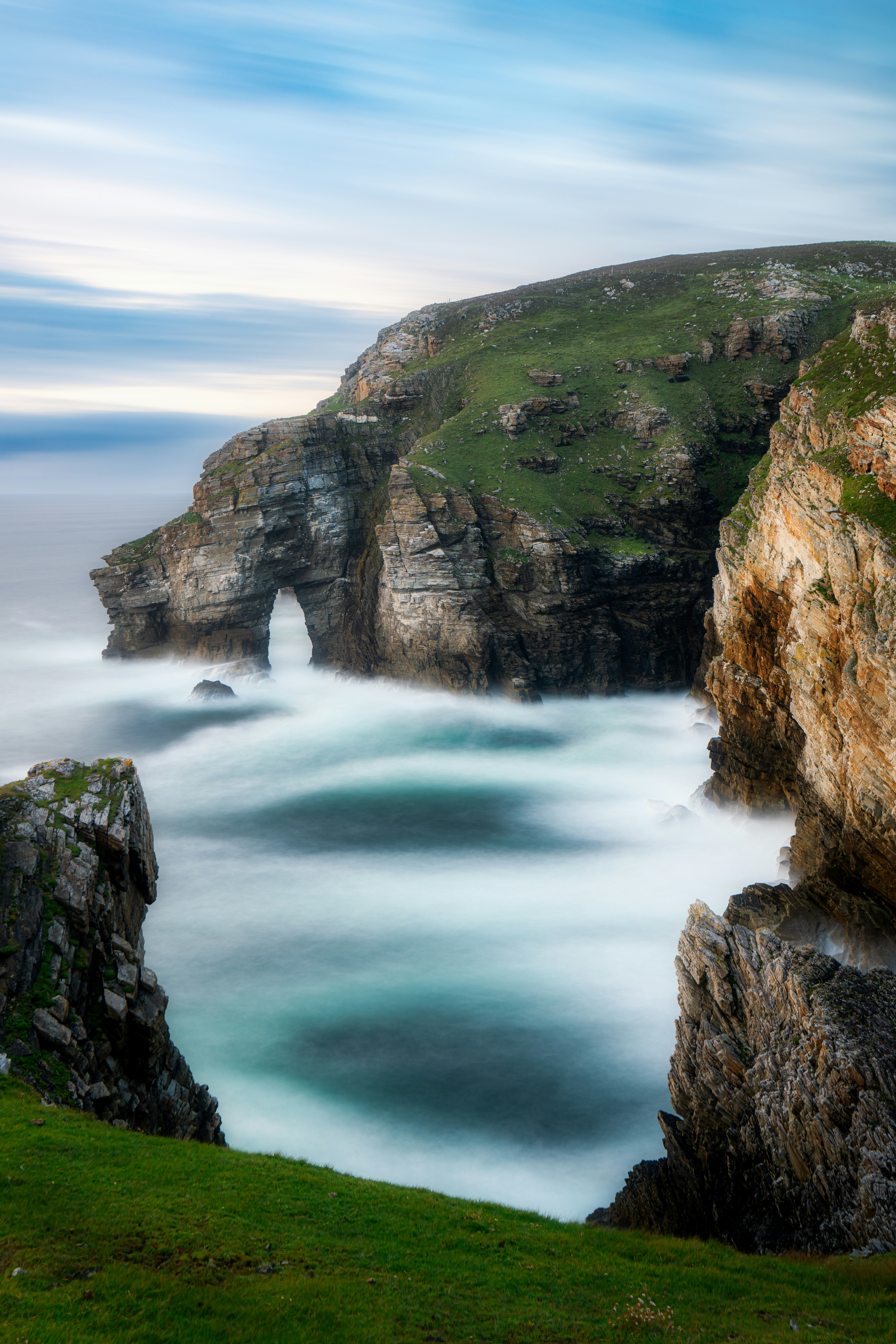 Long exposure of waves crashing against a natural stone arch on a cliff