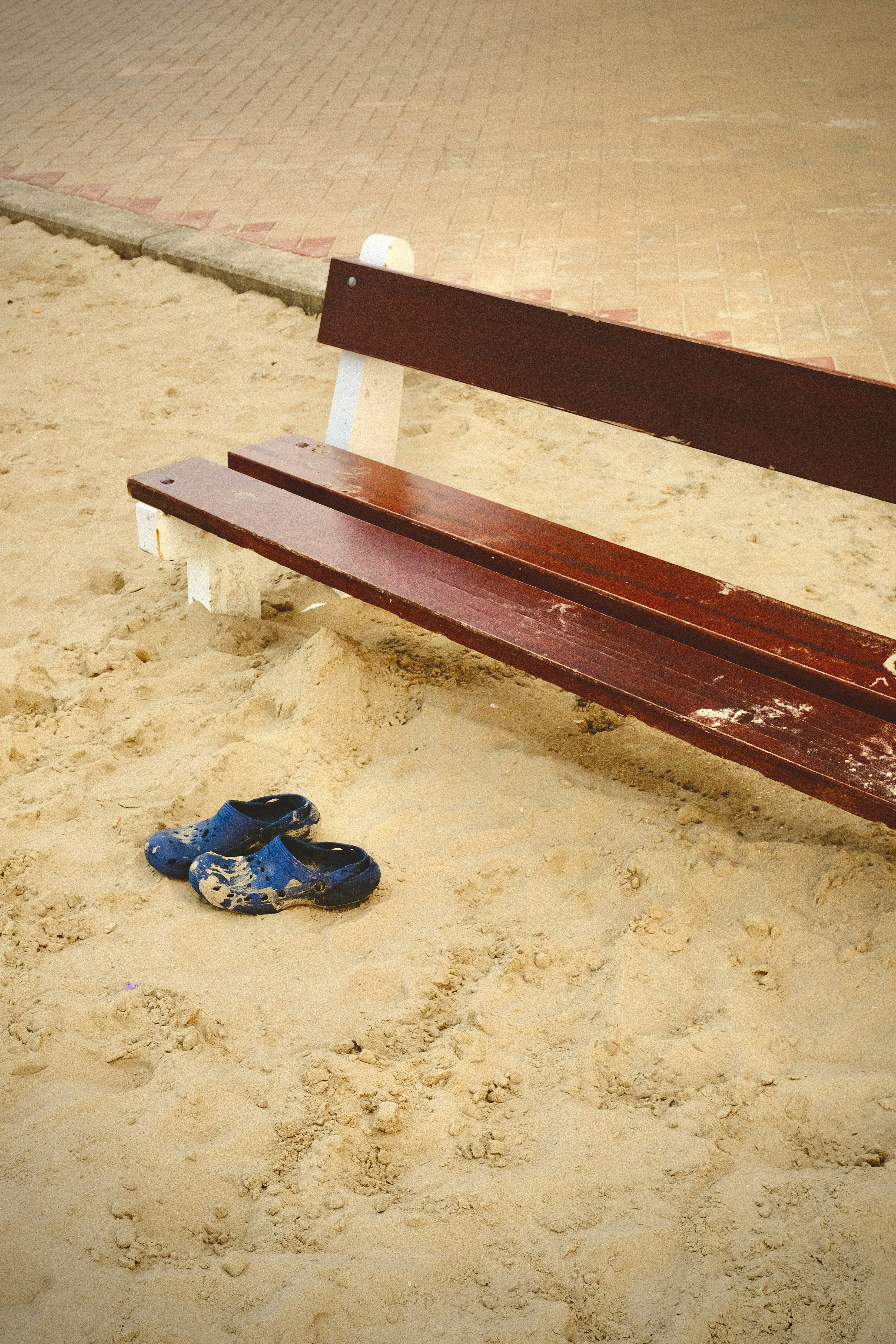 A pair of muddy blue clogs on the sand beside a wooden bench