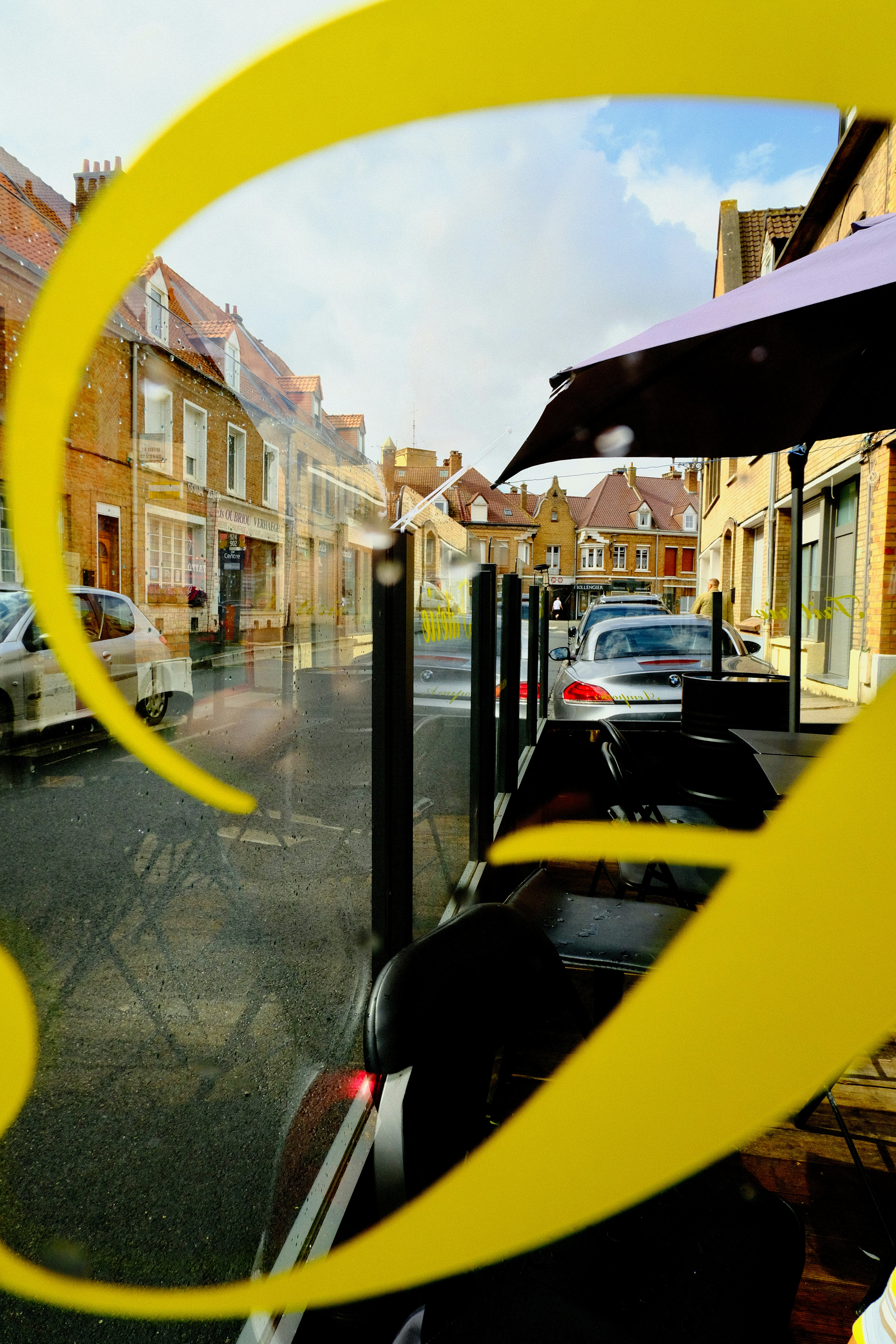 A street view through a glass window with yellow lettering and parked cars