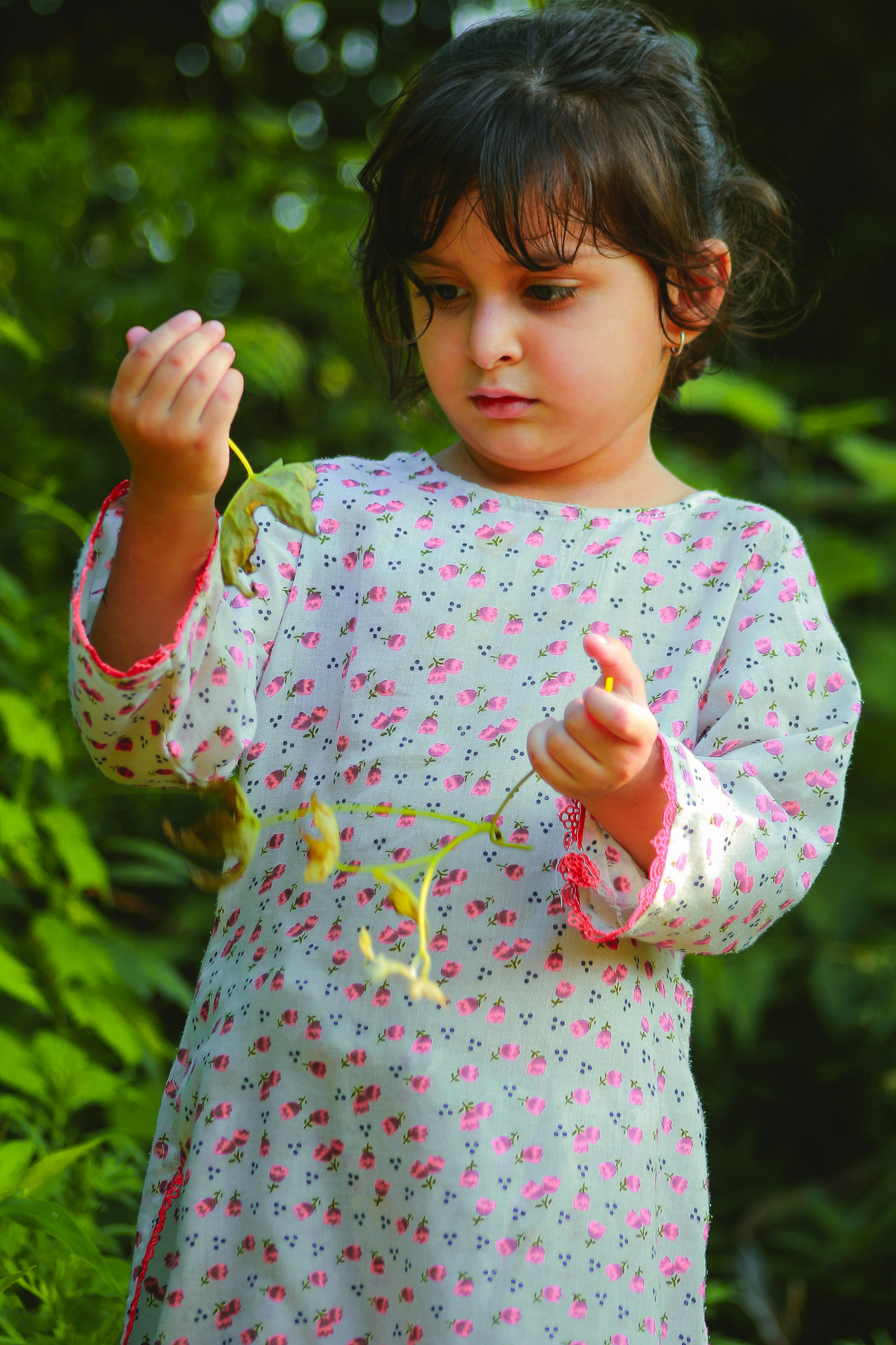 A child in a floral tunic holding a small branch in a garden