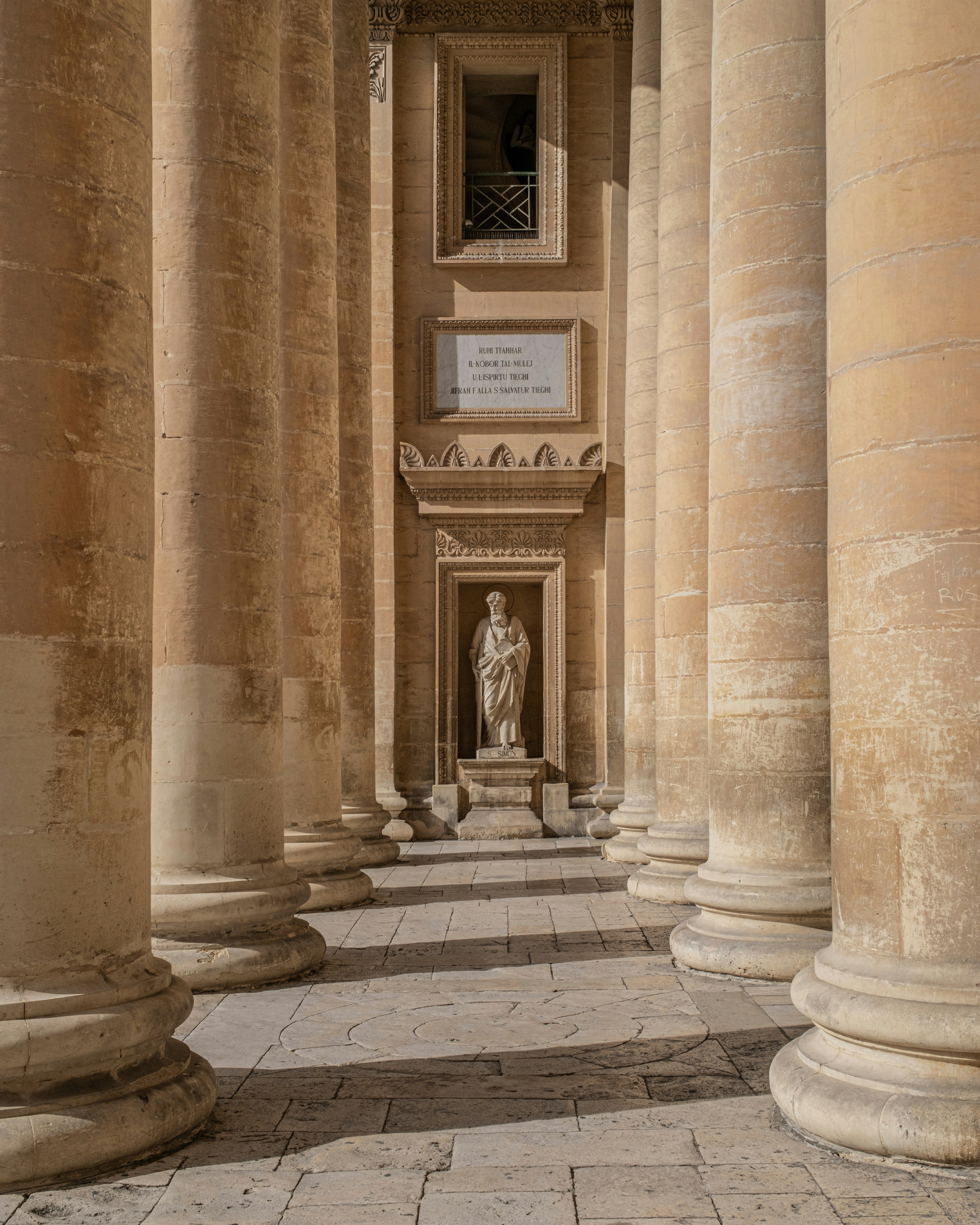 A stone statue of a man in a niche between tall classical columns