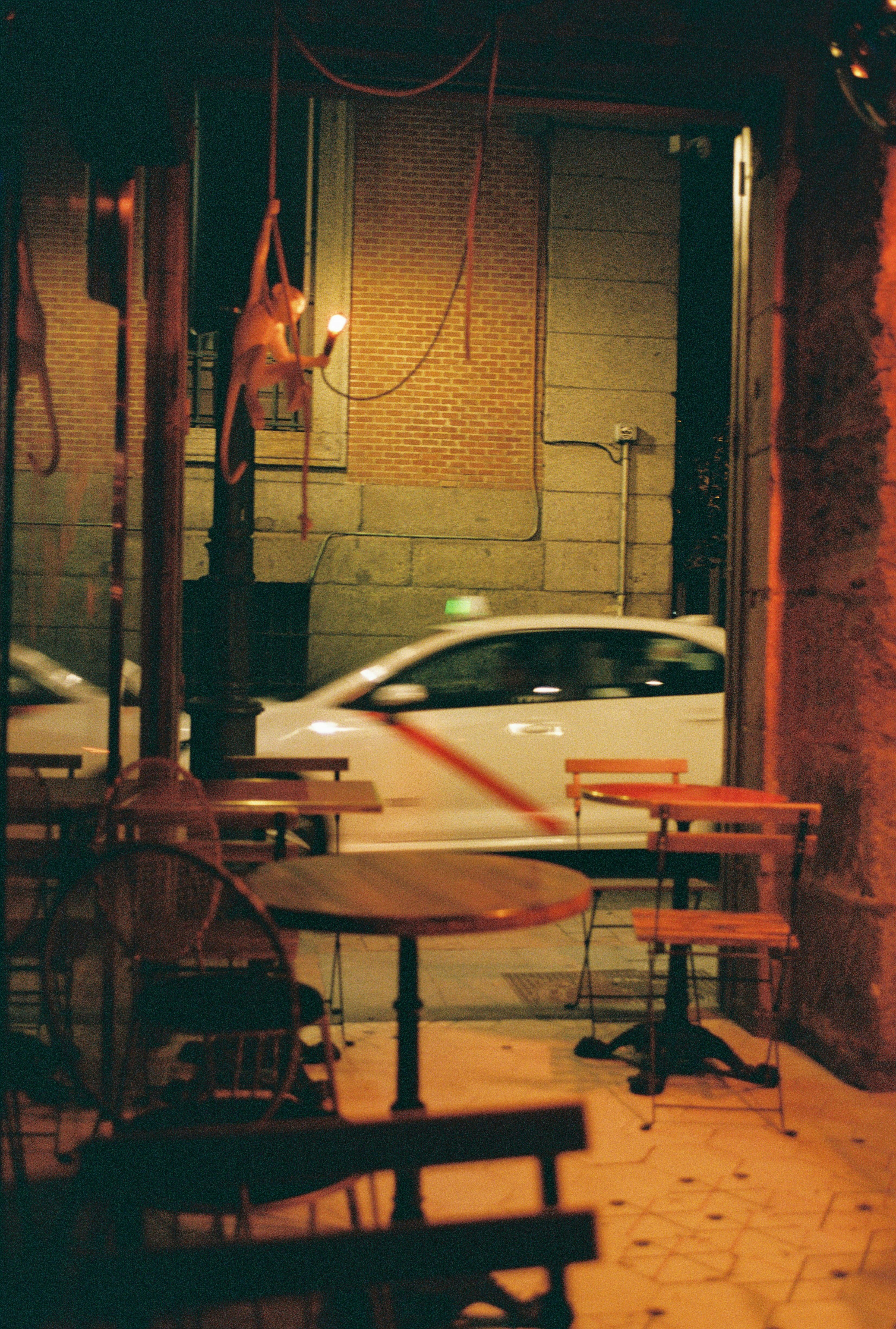 A white taxi driving past a cafe terrace at night in Madrid