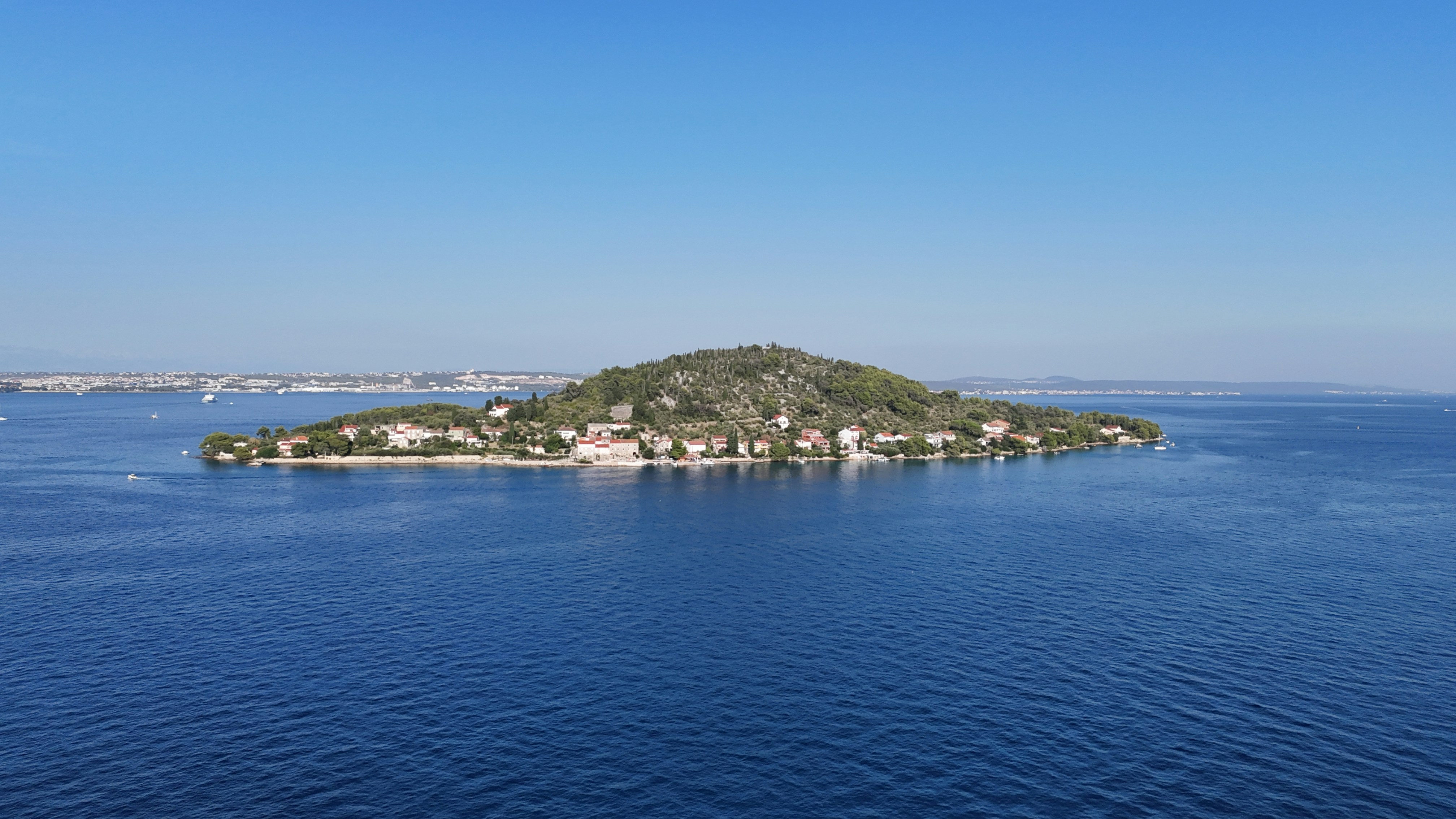A small island with stone houses and trees surrounded by deep blue water