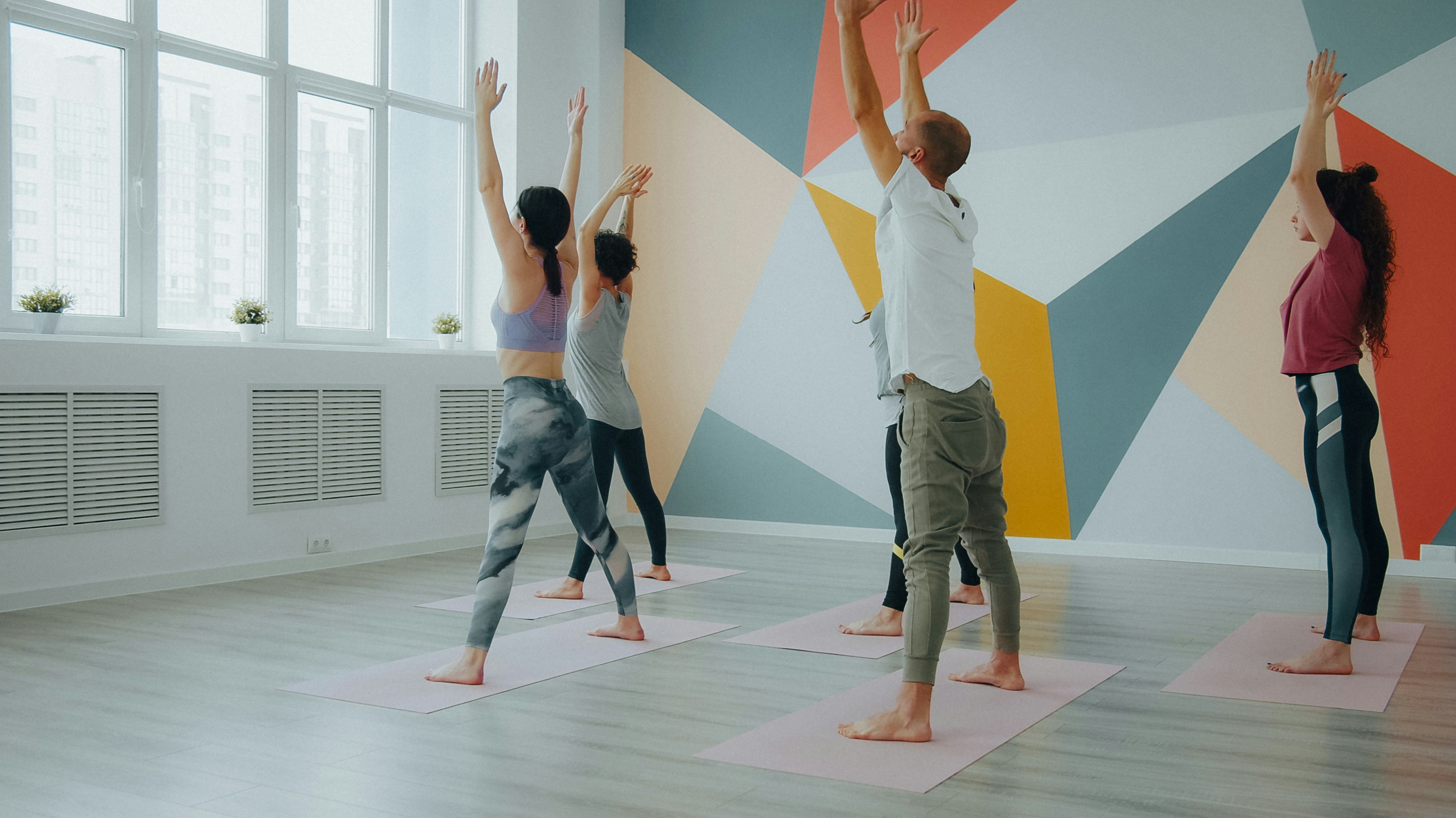A group of people practicing yoga with arms raised in a bright studio