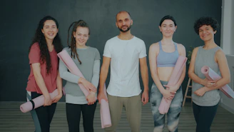 A group of five people holding yoga mats in a studio