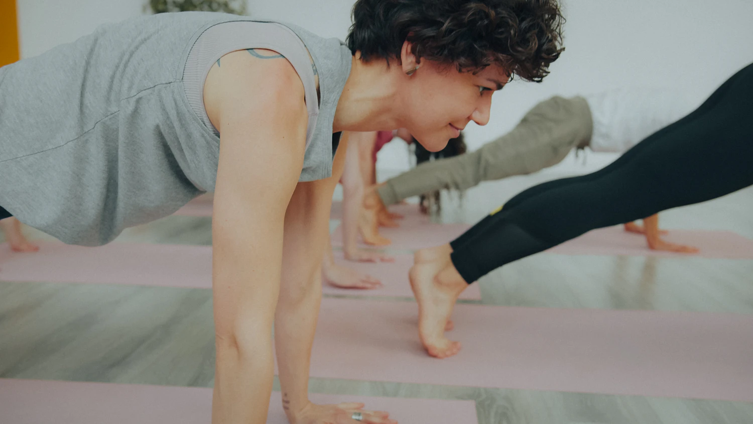 A row of people holding a high plank on pink mats, the nearest one looking down the line
