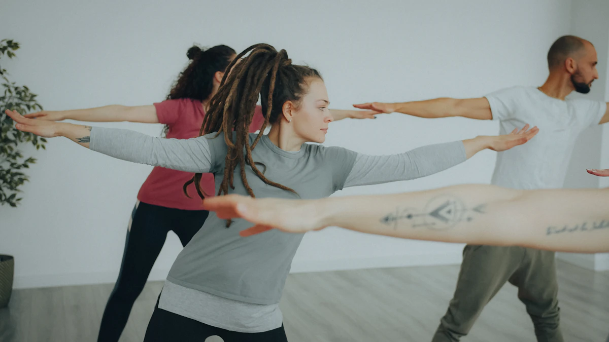 Trois personnes en tenue souple tiennent la même posture, bras tendus à l'horizontale, dans une salle claire au parquet de bois avec une plante verte