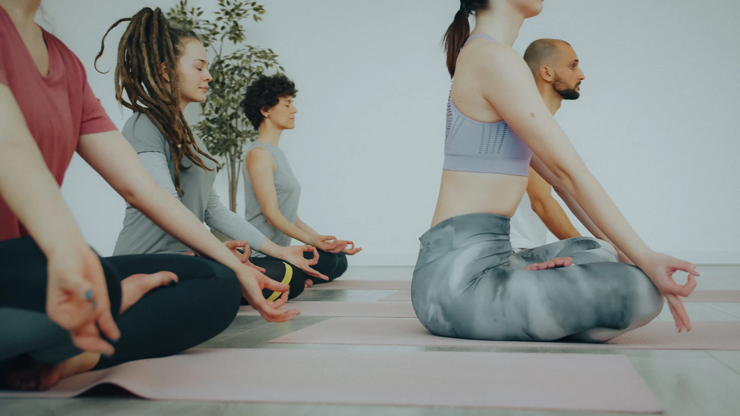 A row of people sitting on mats in a bright room, the nearest one folding forward over her legs