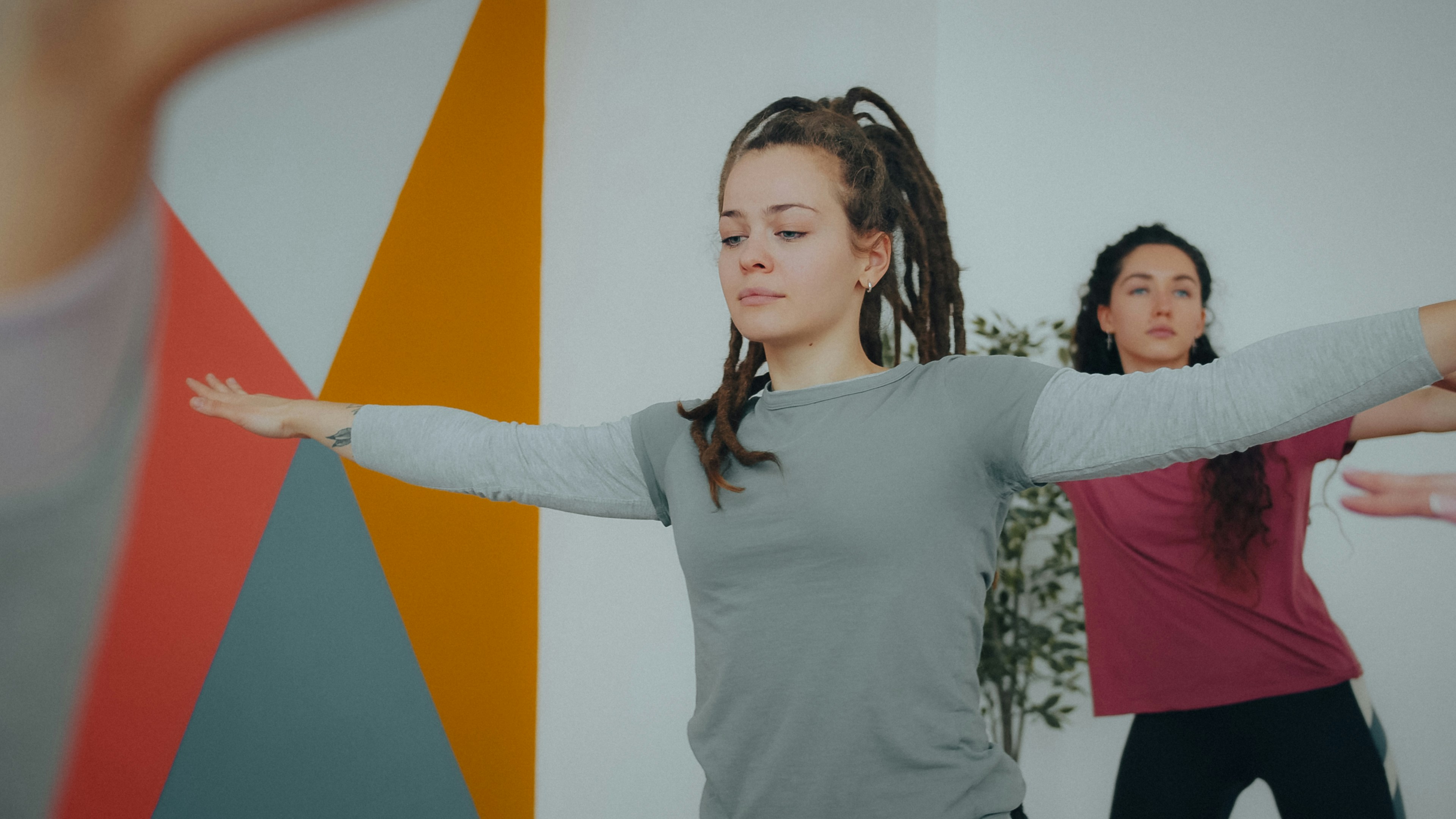 Two women in a studio with geometric wall art practicing yoga poses
