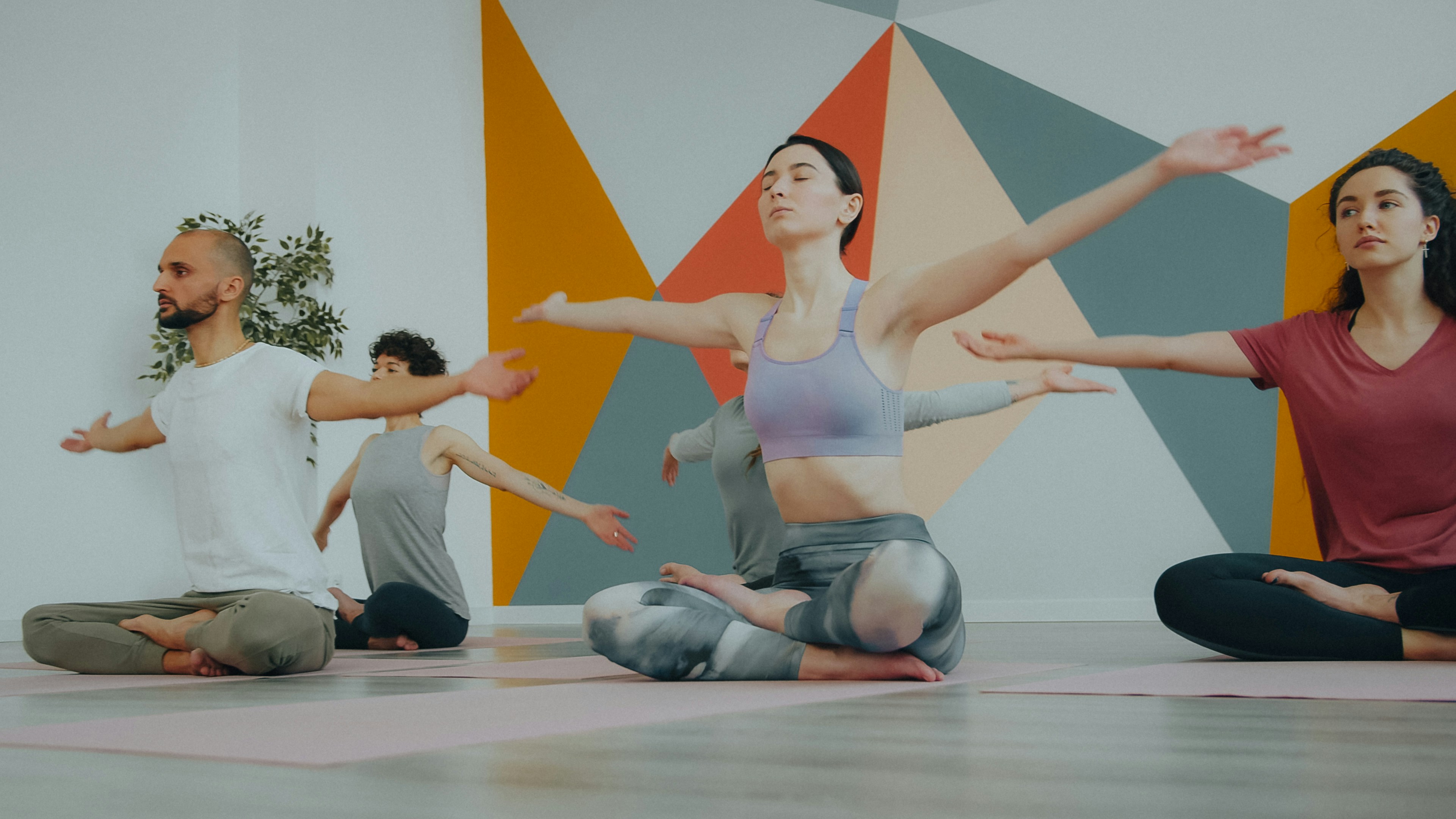 A group of people sitting in lotus position with arms outstretched in a yoga studio