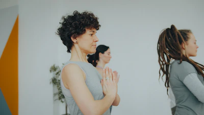 Three people in a row with hands pressed together in a yoga studio