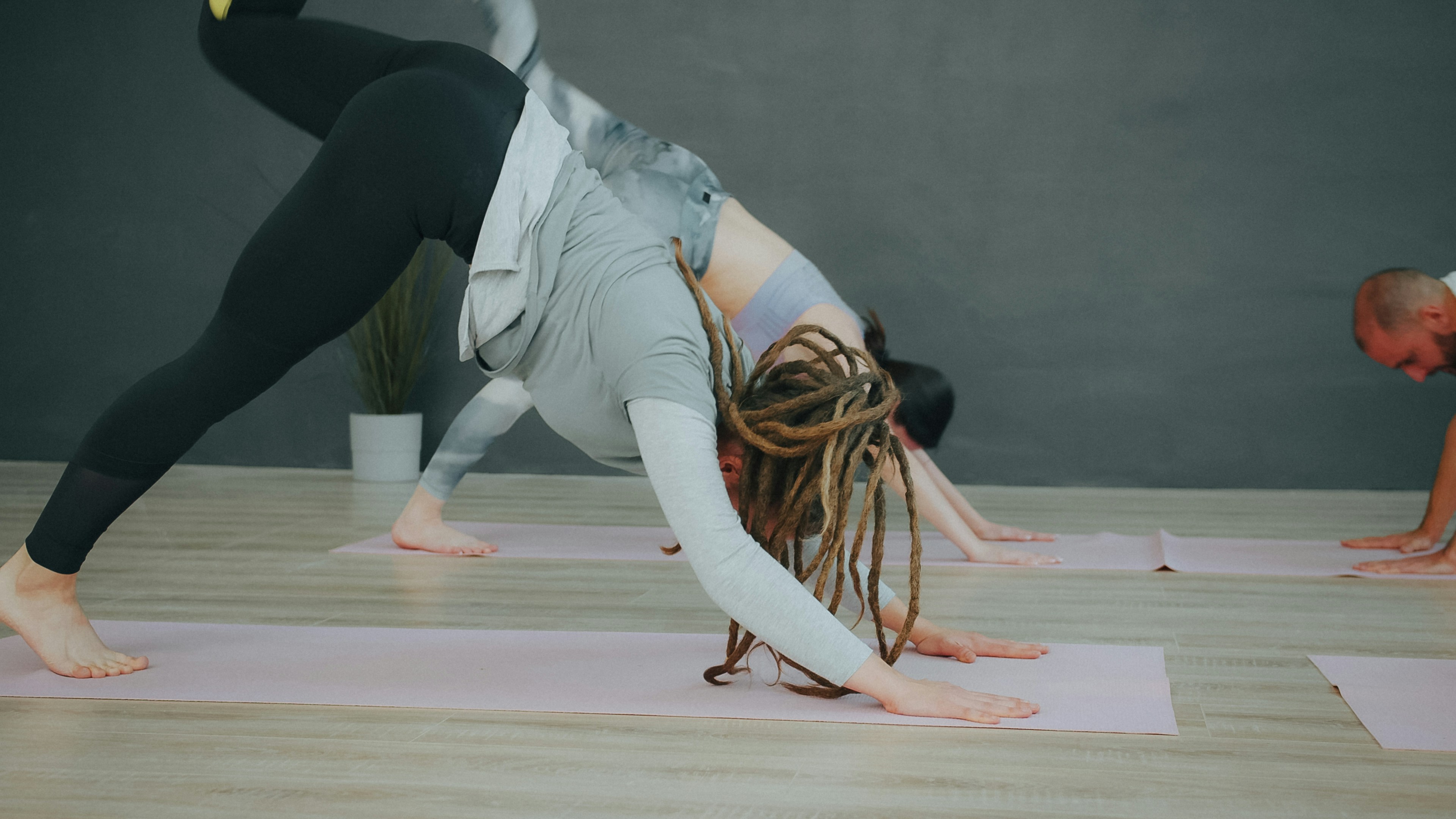 People in a yoga class performing a three-legged downward dog pose on mats