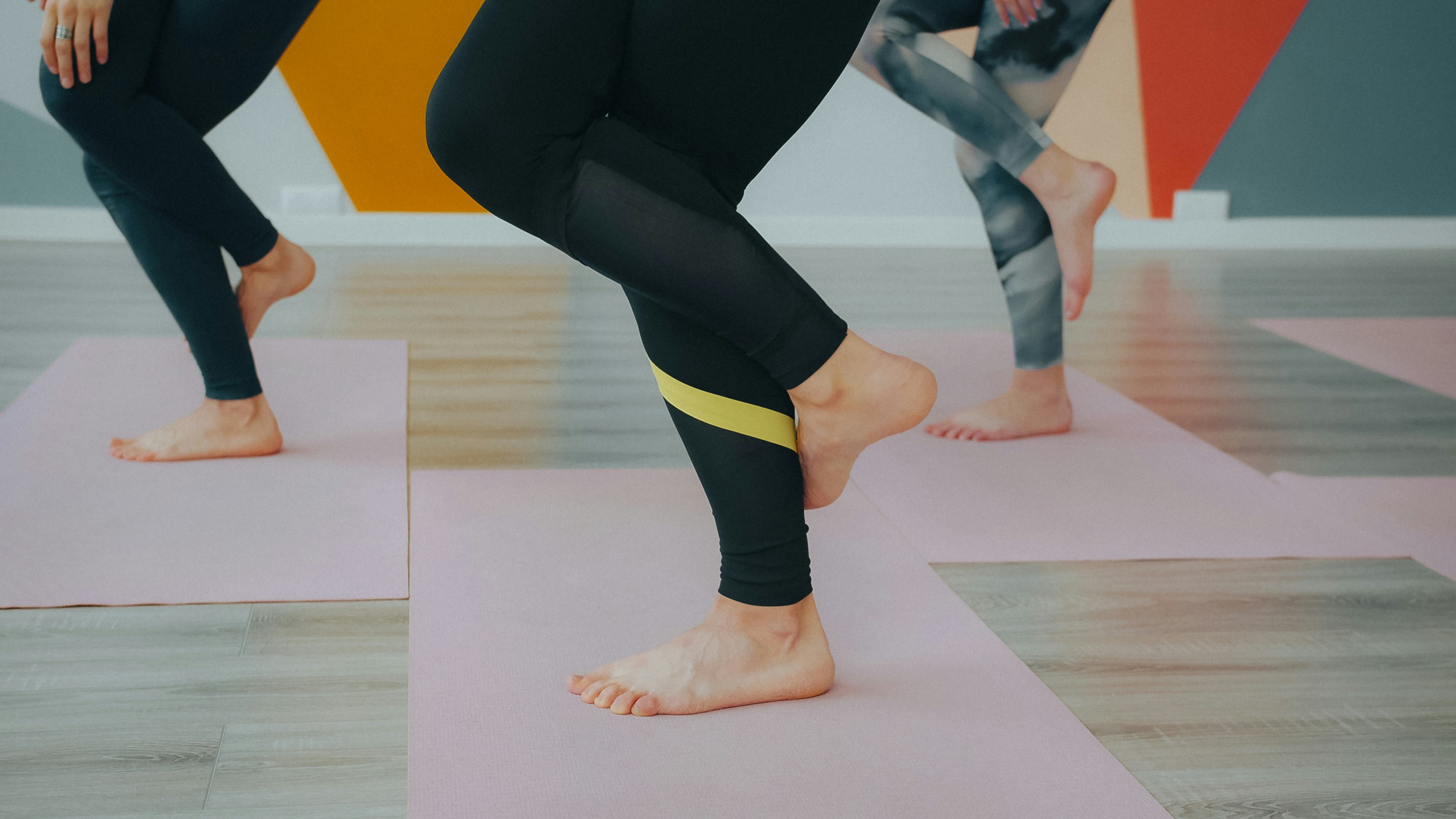 People in leggings balancing on one leg on pink yoga mats in a studio