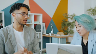 A man and a woman with teal hair working together in a colorful office