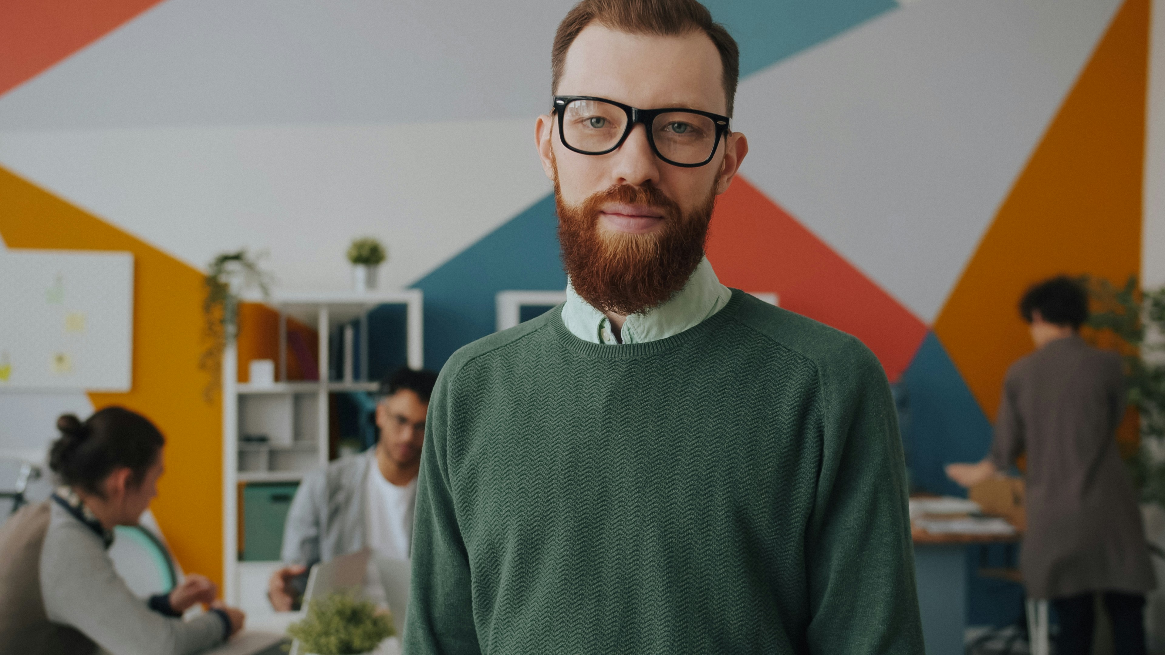 A man with a red beard and glasses in a green sweater in an office