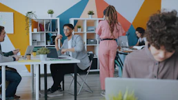 People working in a colorful office with geometric wall patterns and white shelving