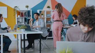 People working in a colorful office with geometric wall patterns and white shelving