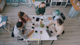 A group of five people collaborating around a white table in a workspace