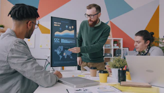 A man pointing at a vertical monitor displaying data charts to two colleagues