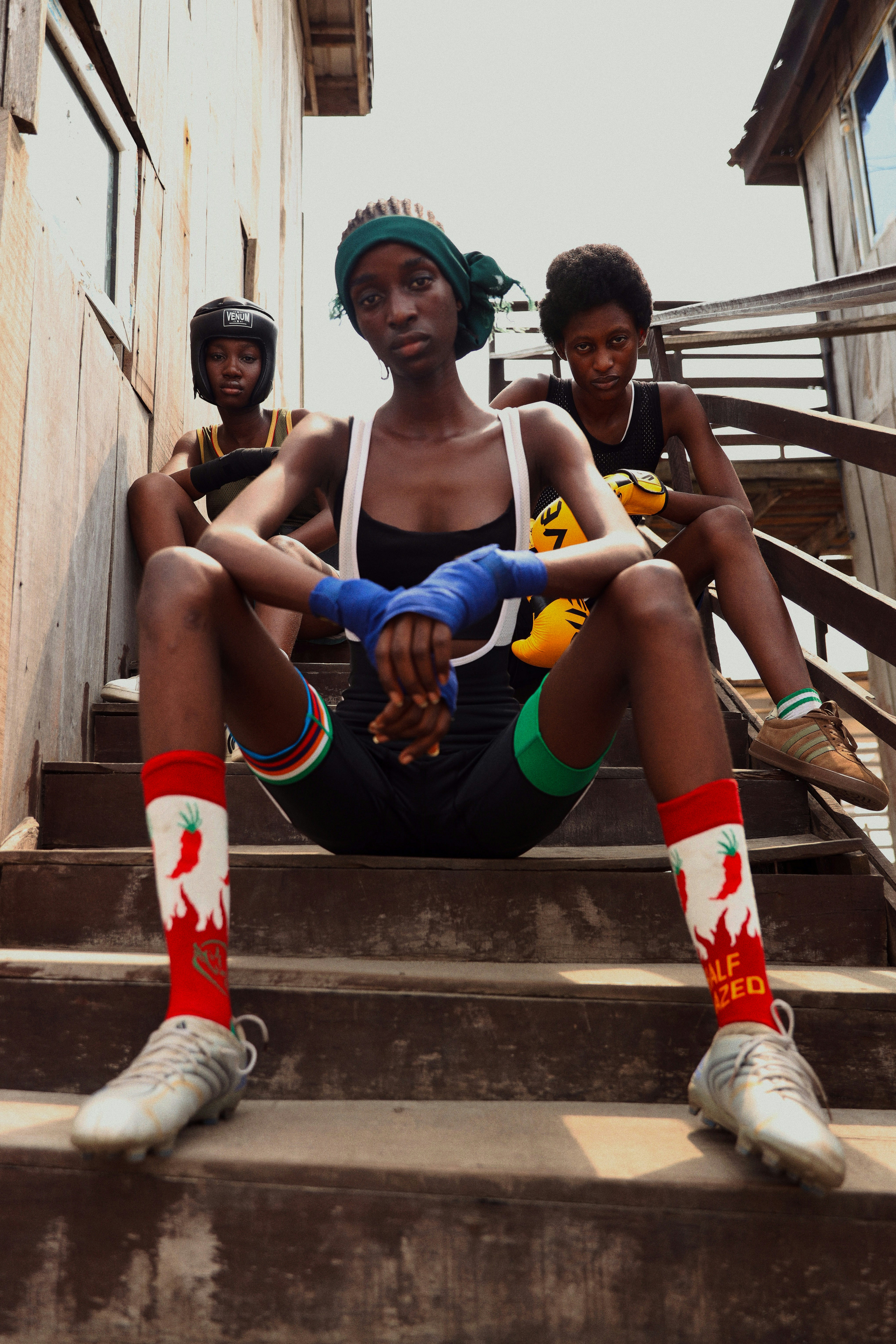 Three people in athletic gear sitting on wooden stairs, wearing boxing gloves and wraps