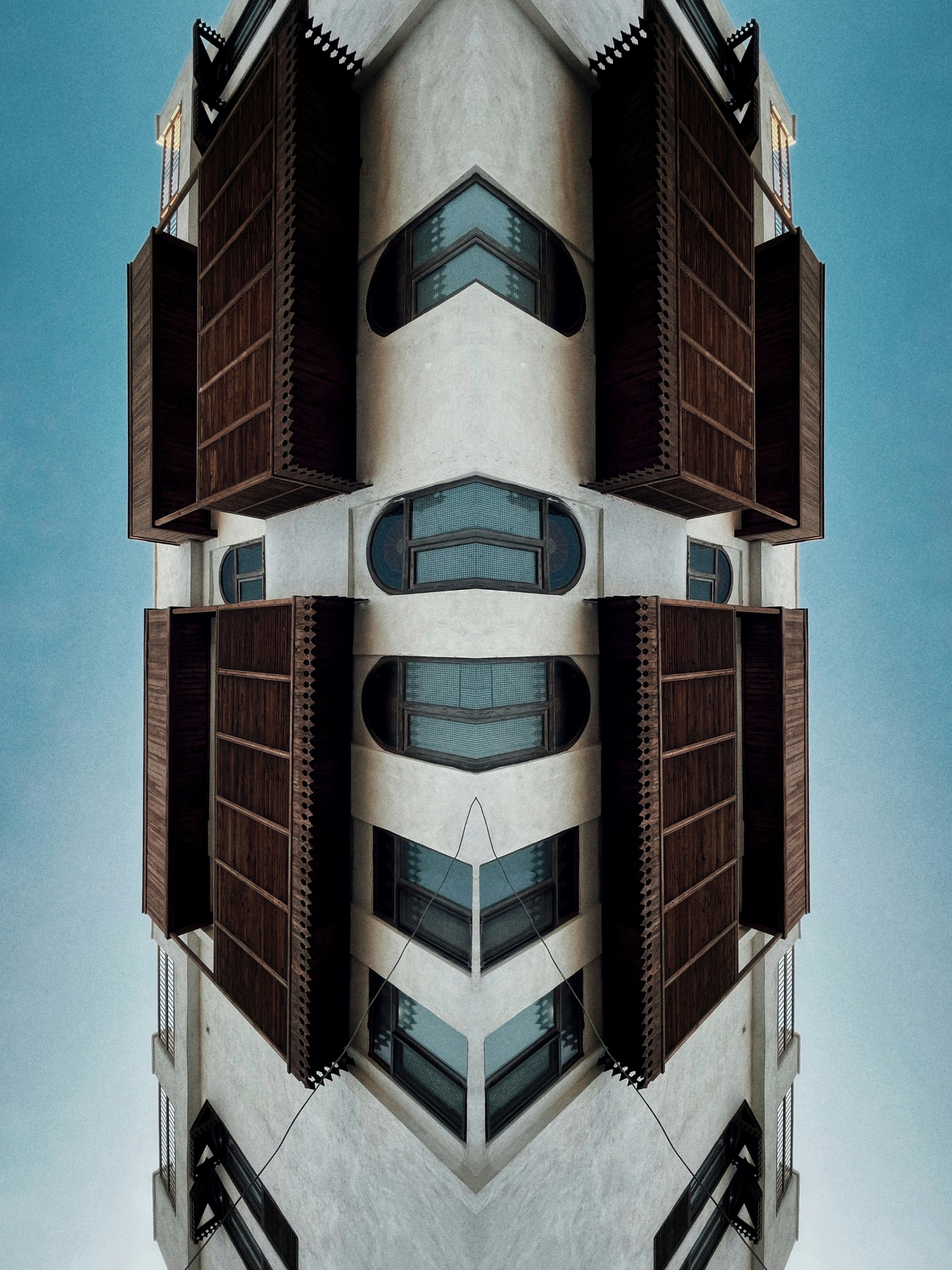 A symmetrical building facade with wooden shutters and windows against a blue sky