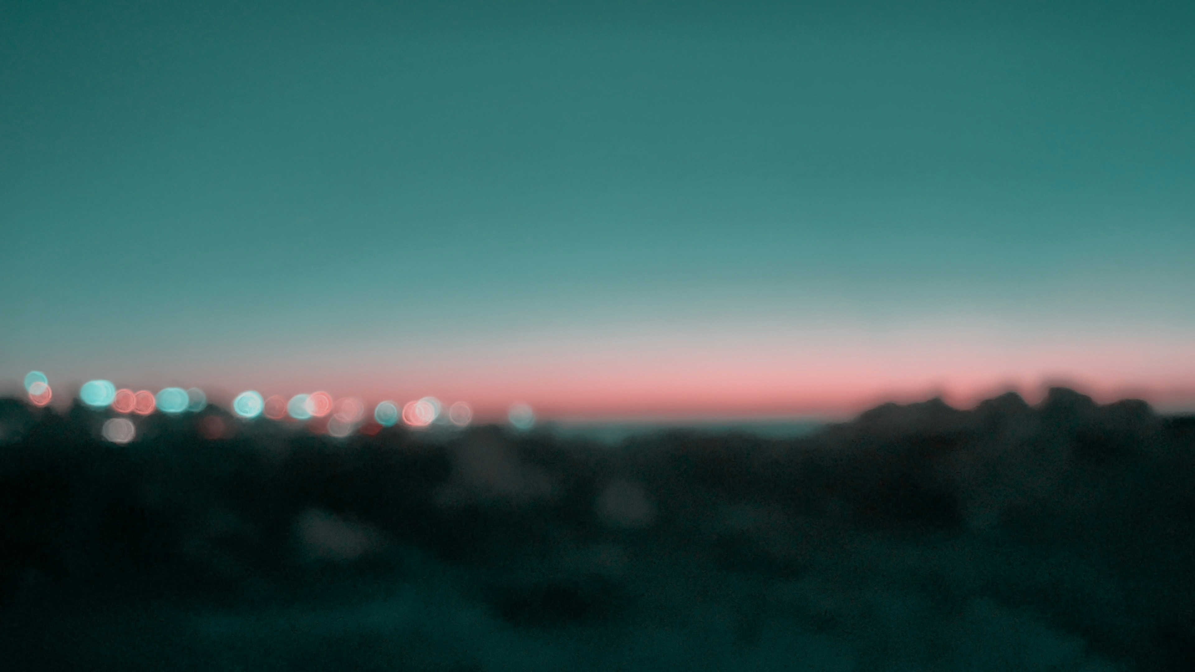 Blurred city lights glowing against a soft pink and teal horizon