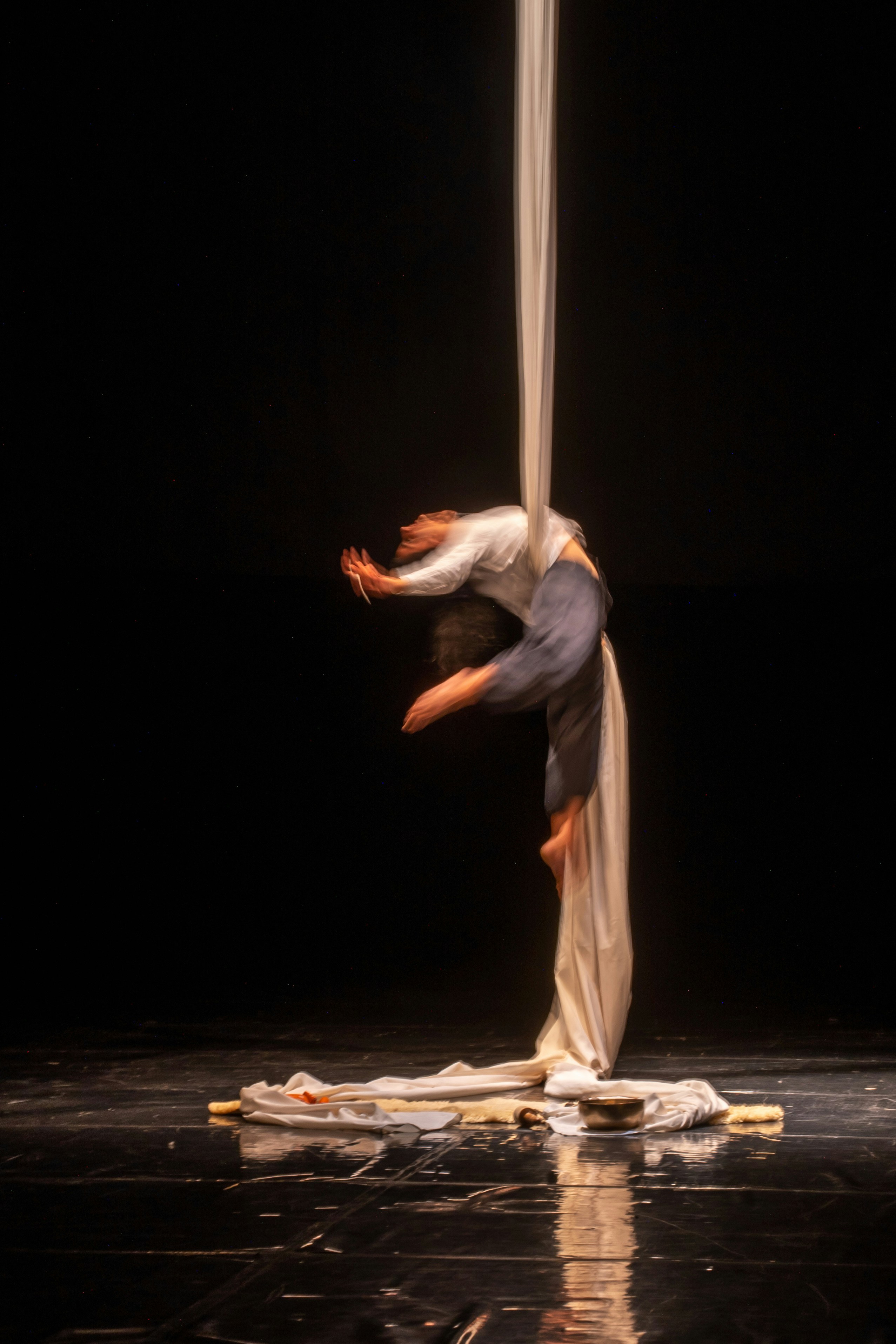 A person performing aerial silks in a long exposure against a black background