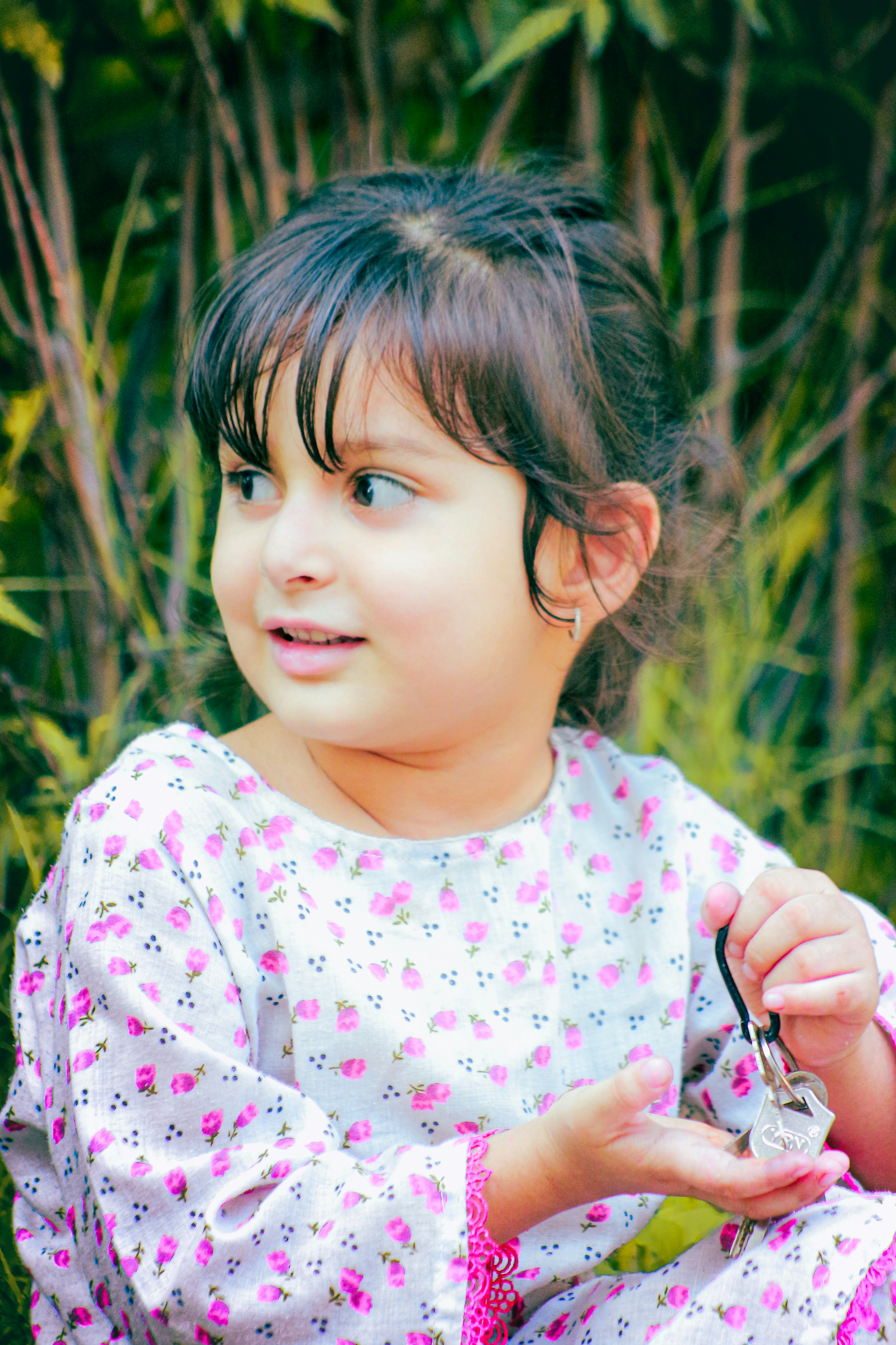 A child in a floral print shirt holding a set of keys outdoors