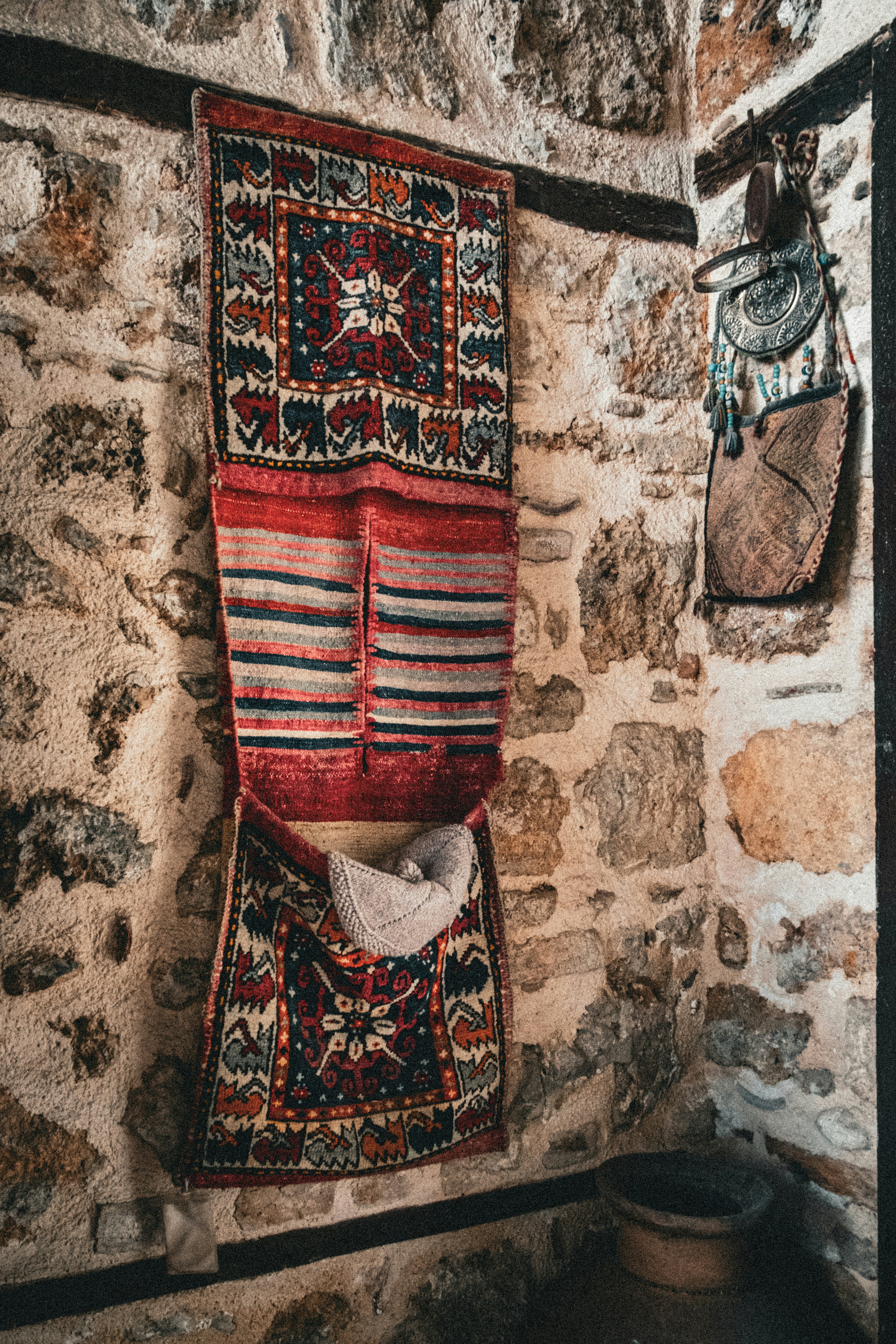Un textile tissé à motifs accroché à un mur rustique de pierre avec une pochette en cuir