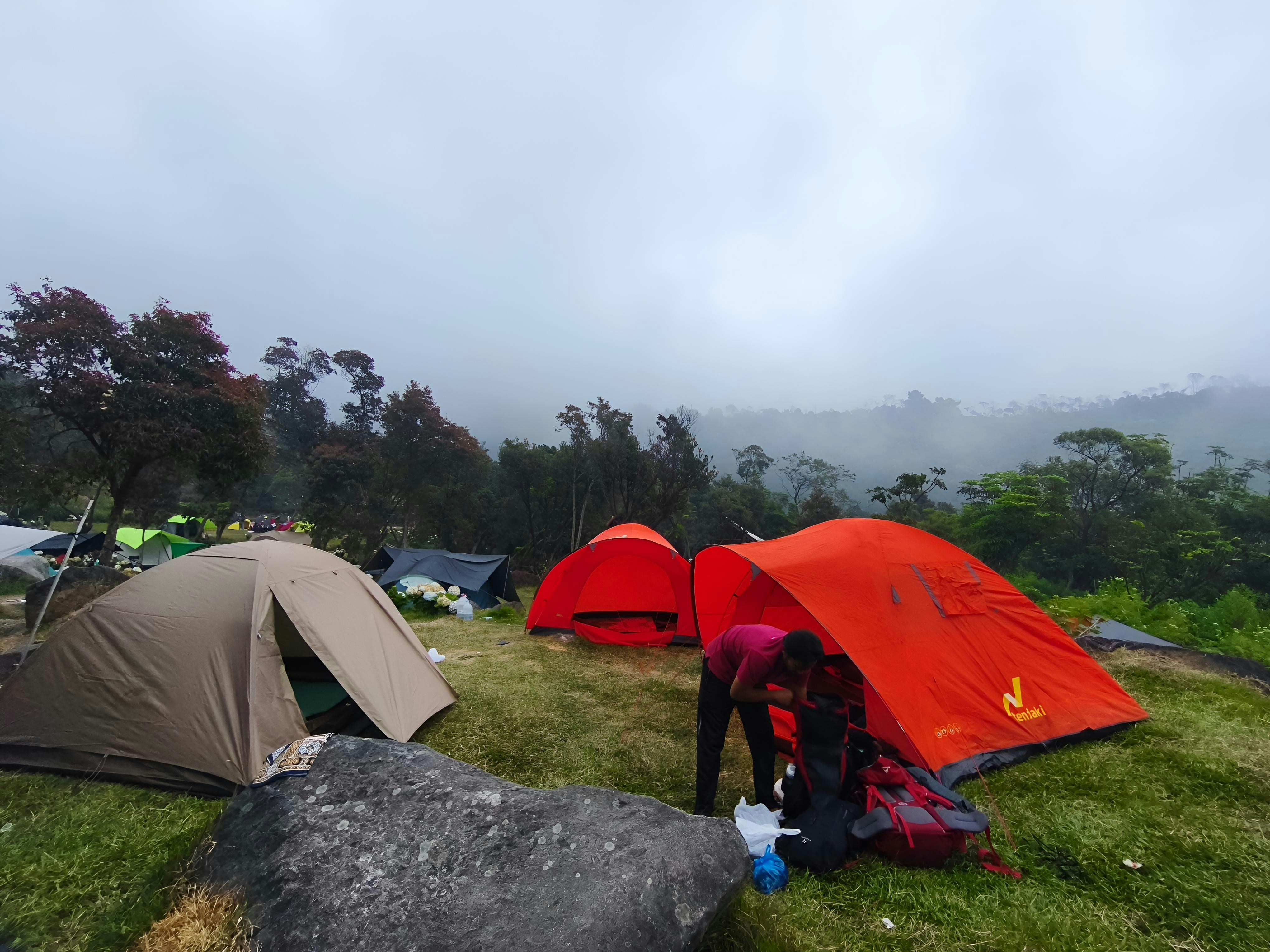 A person packing a backpack by an orange tent in a misty mountain campsite