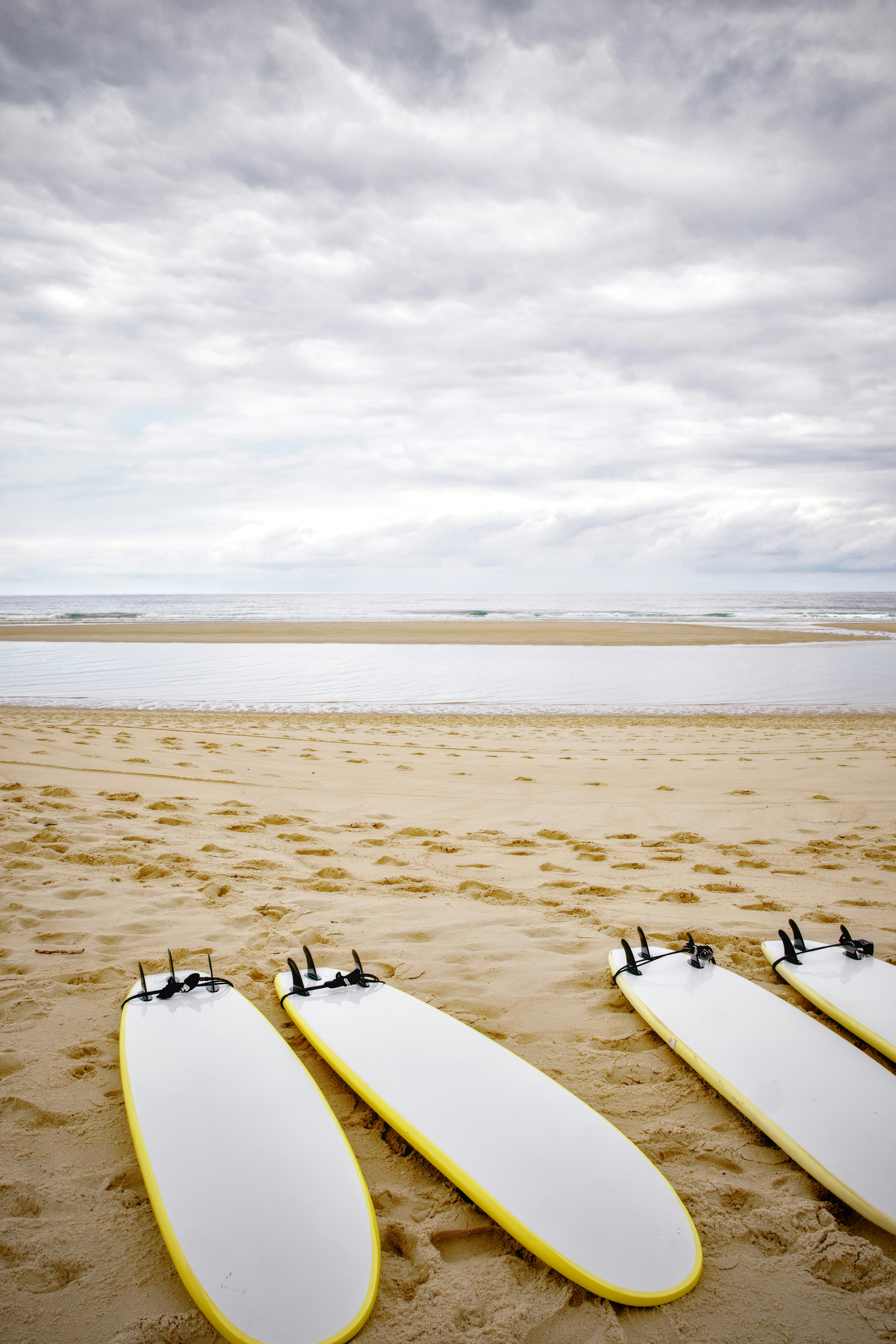 Three white surfboards resting on a sandy beach under a cloudy sky