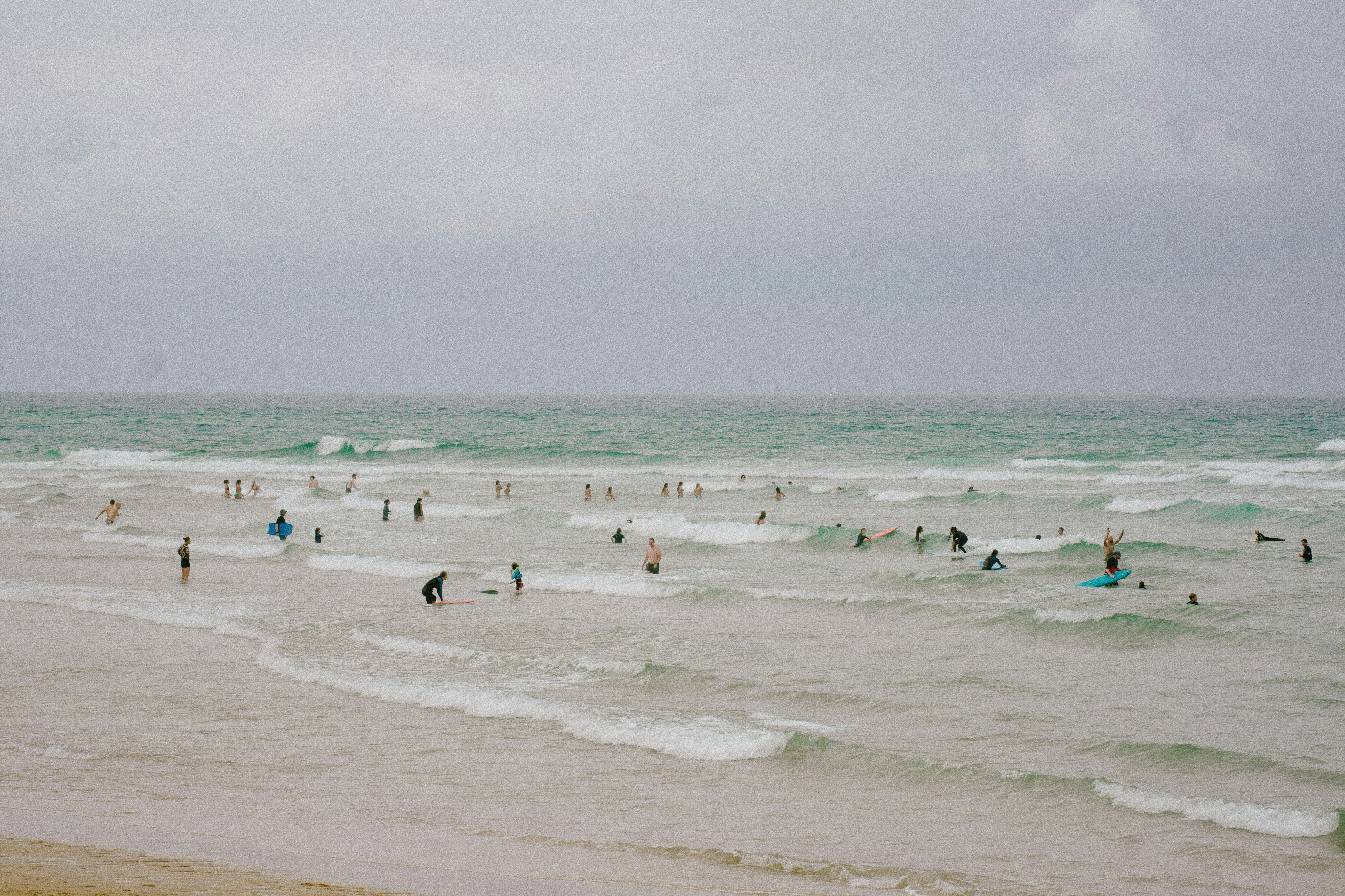 A group of people with surfboards and bodyboards in the ocean under cloudy skies