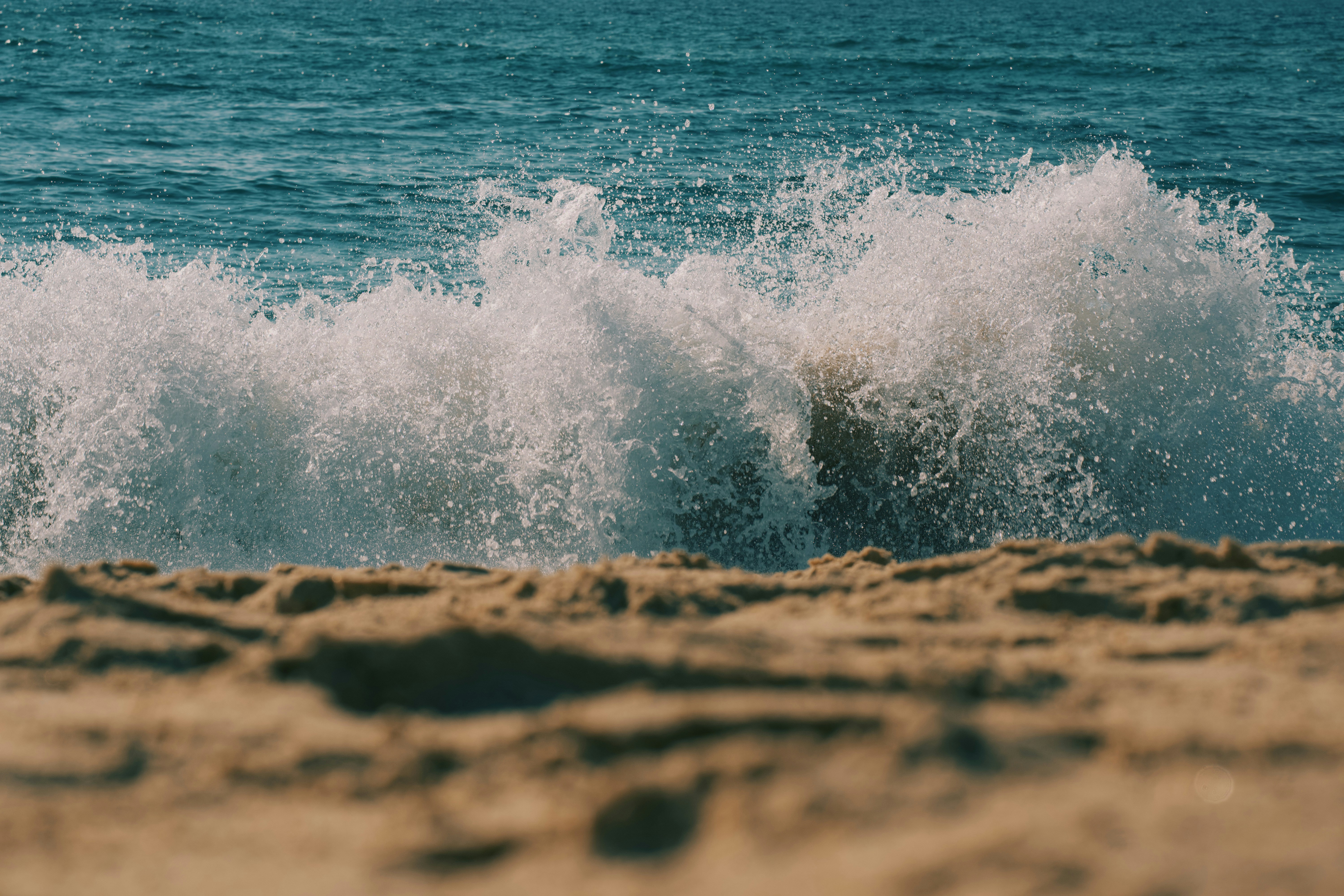 A white ocean wave crashing onto a sandy beach
