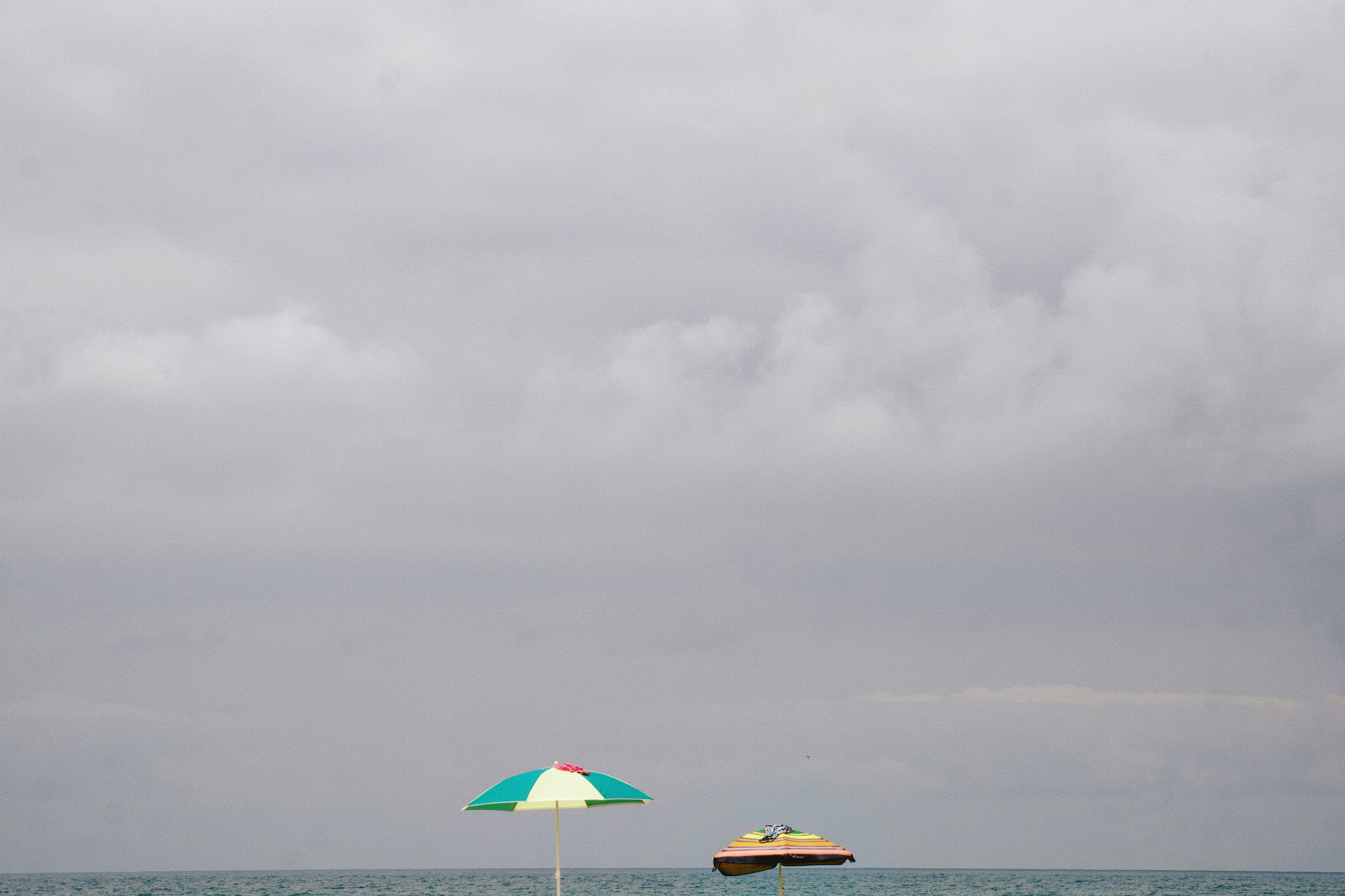 Two beach umbrellas on the horizon under a vast overcast grey sky