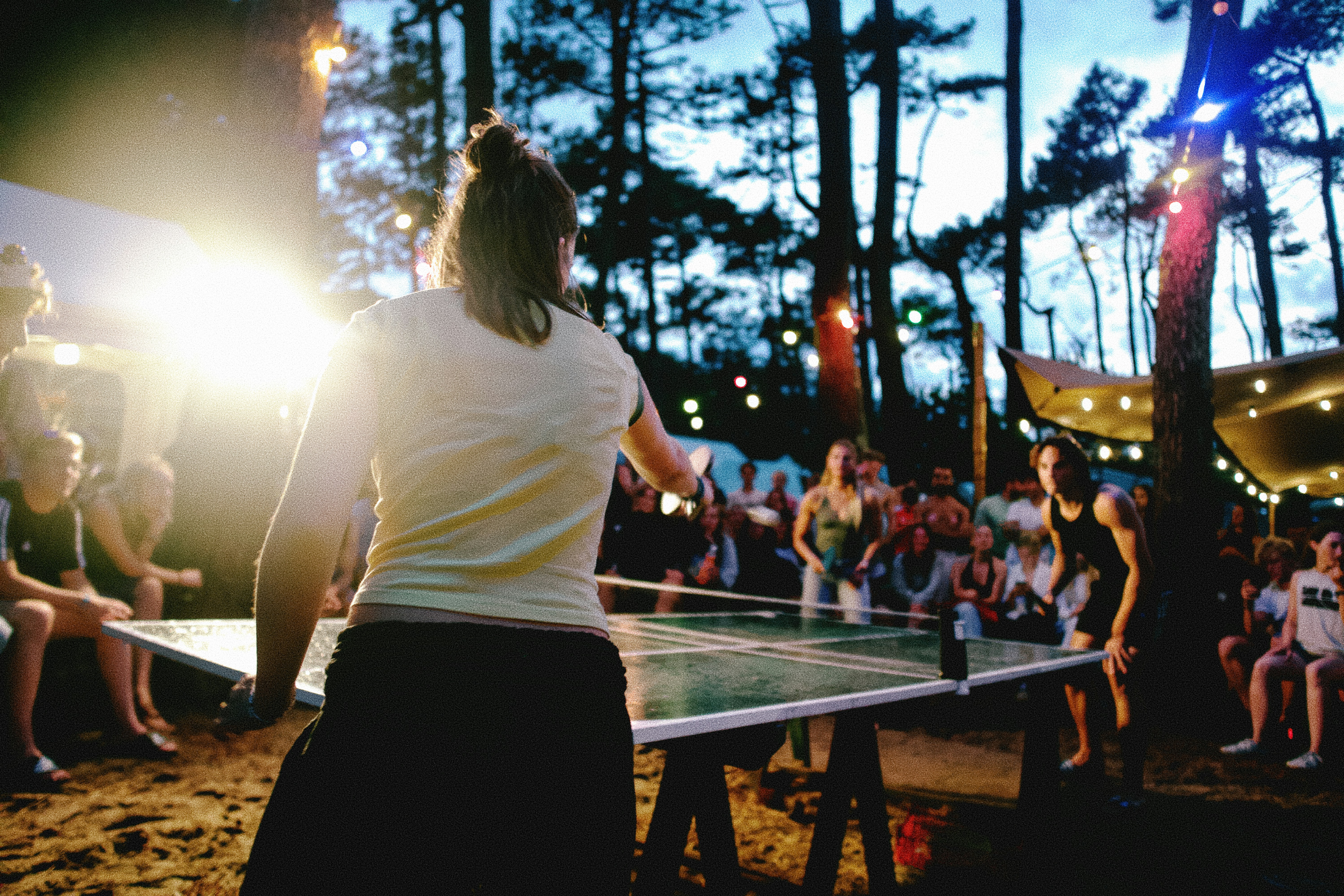 A woman playing table tennis against a man in a forest at night