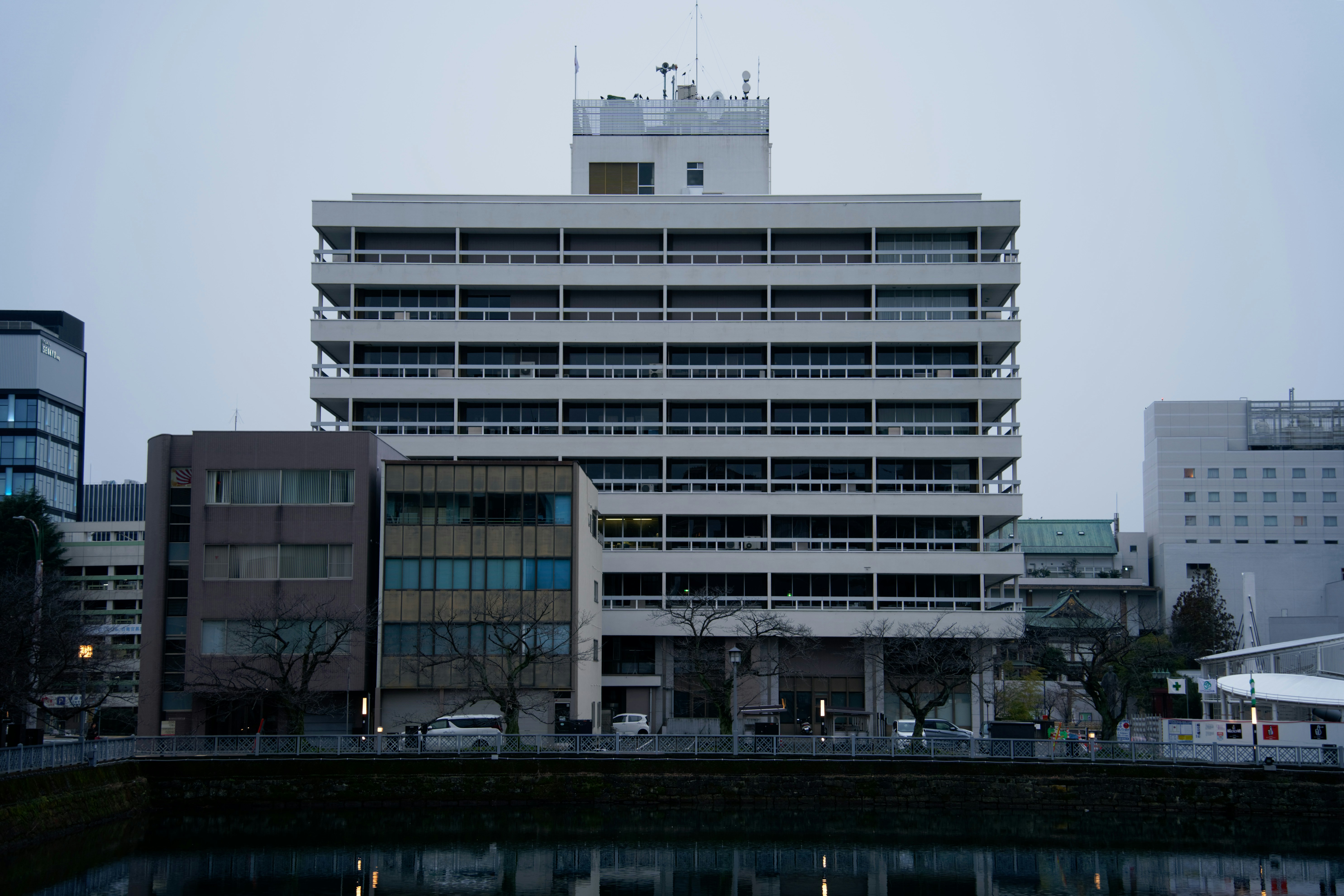 A large white office building behind a canal in a city