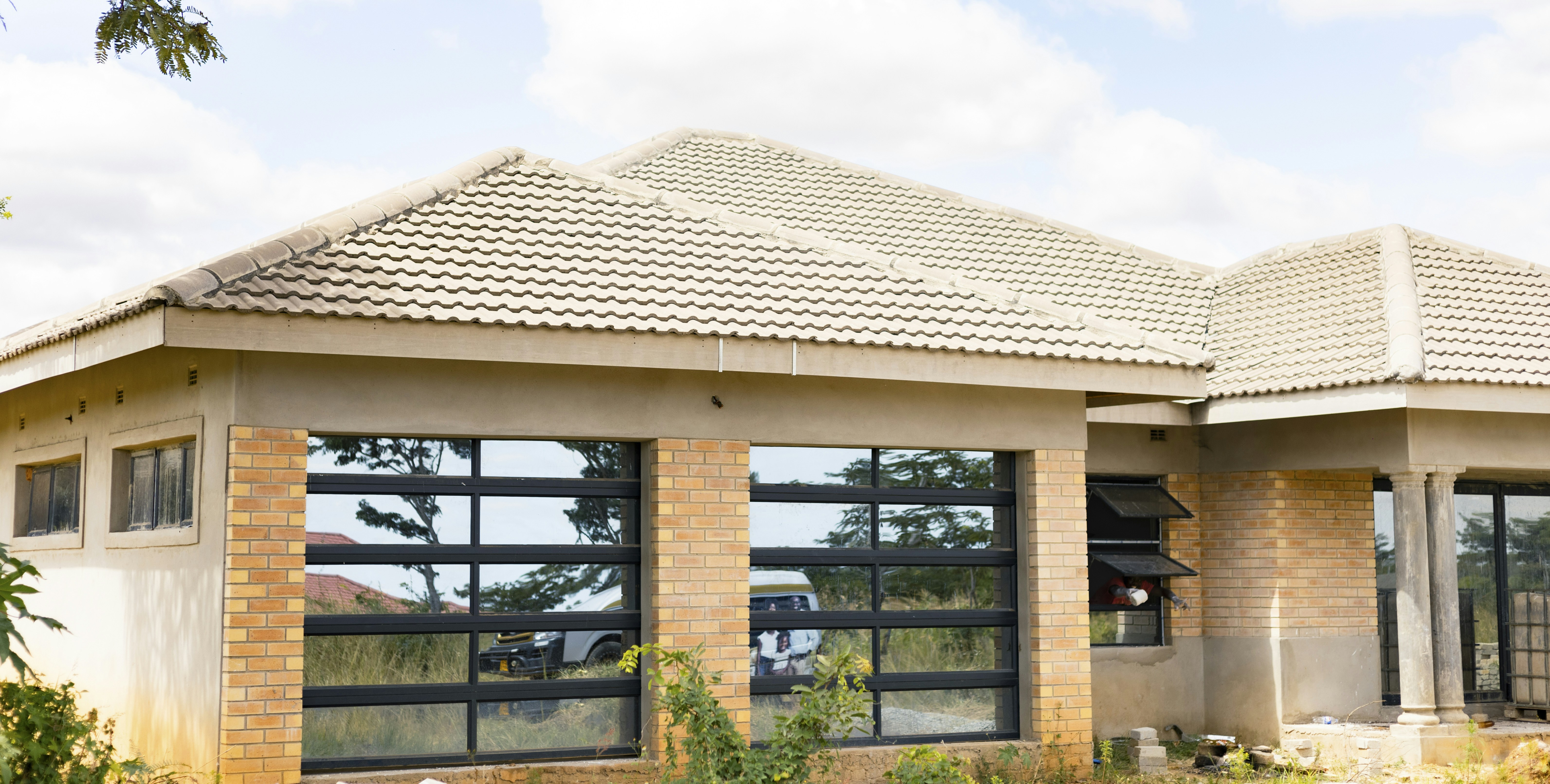 A single-story house with brick pillars and large glass windows under a tiled roof