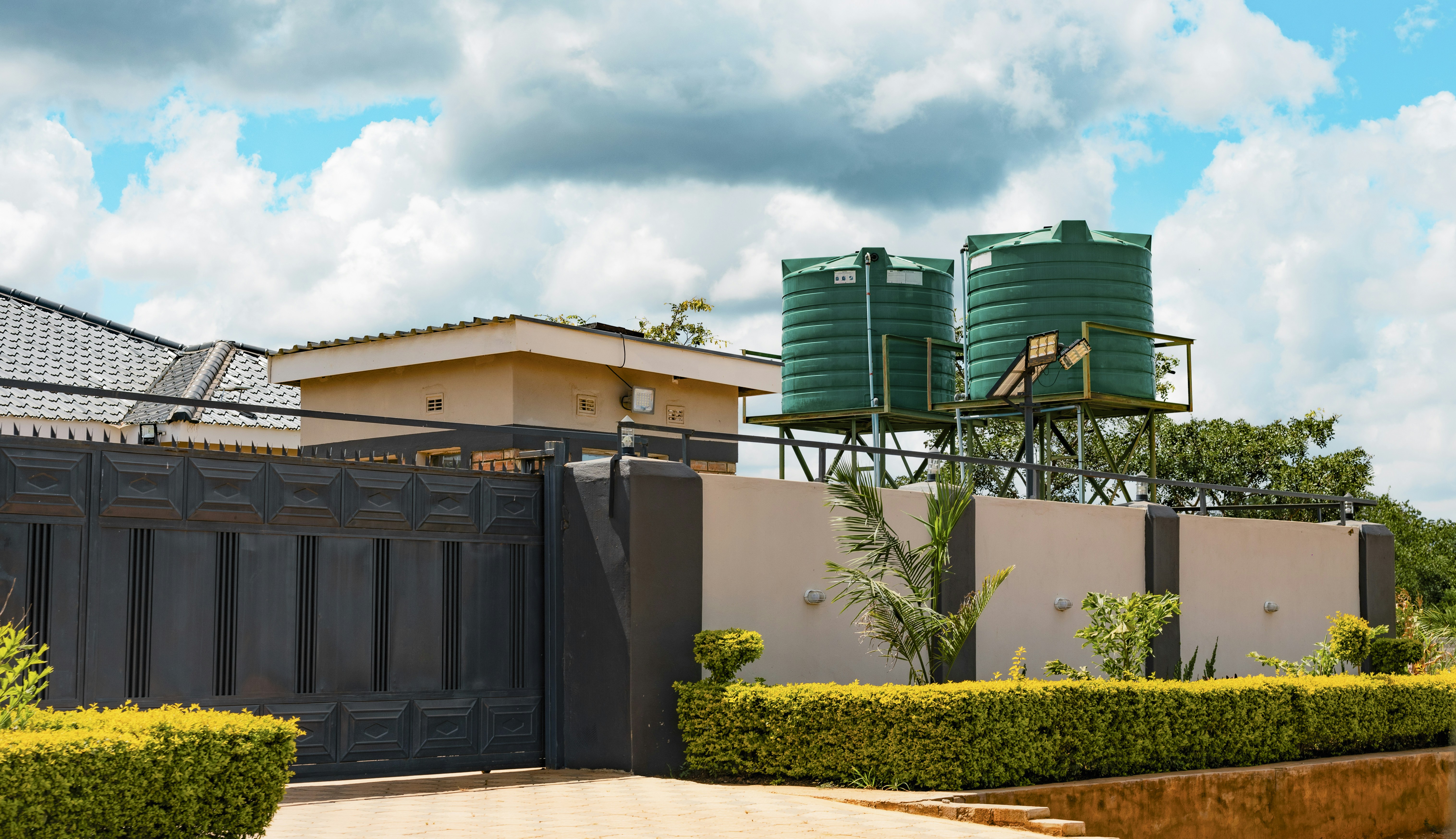 Two green water tanks on metal stands behind a beige wall and gate