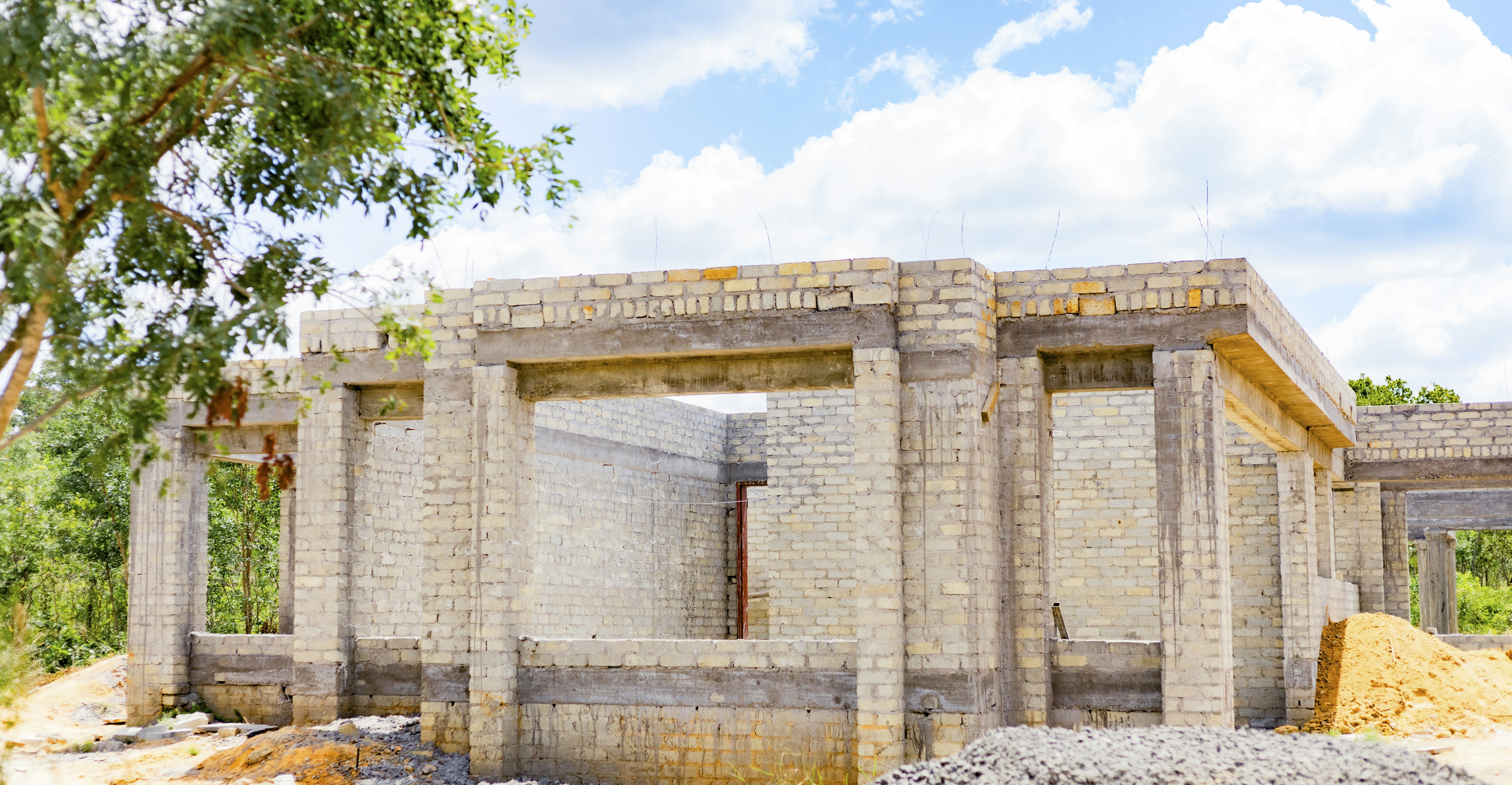 A house under construction with light brick walls and concrete pillars under a blue sky