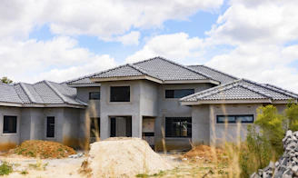 A house under construction with grey tiled roof and unfinished concrete walls