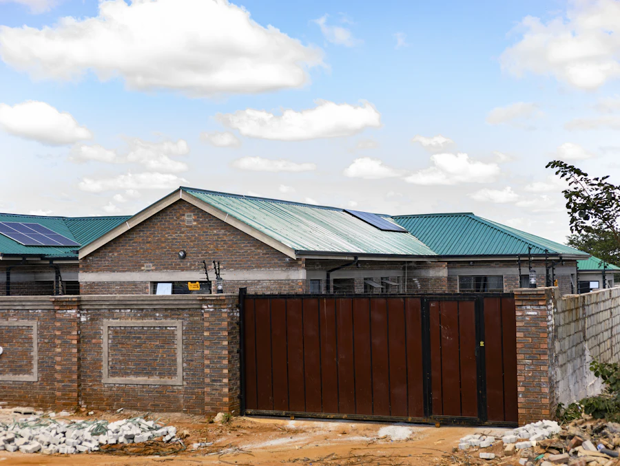 A closed steel gate set into a brick boundary wall, with electric fencing strung above it.