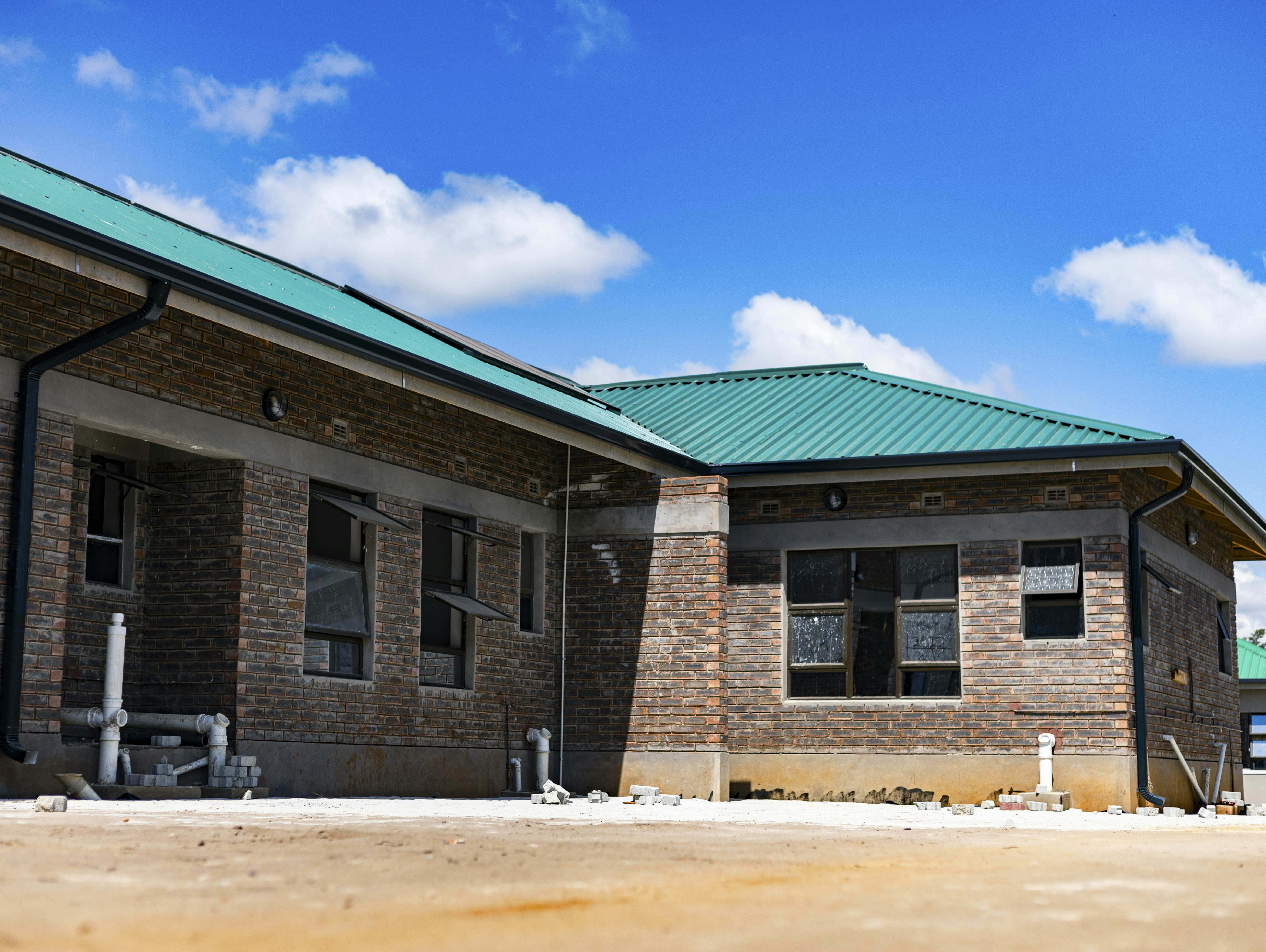 A brick building with a green metal roof under a bright blue sky