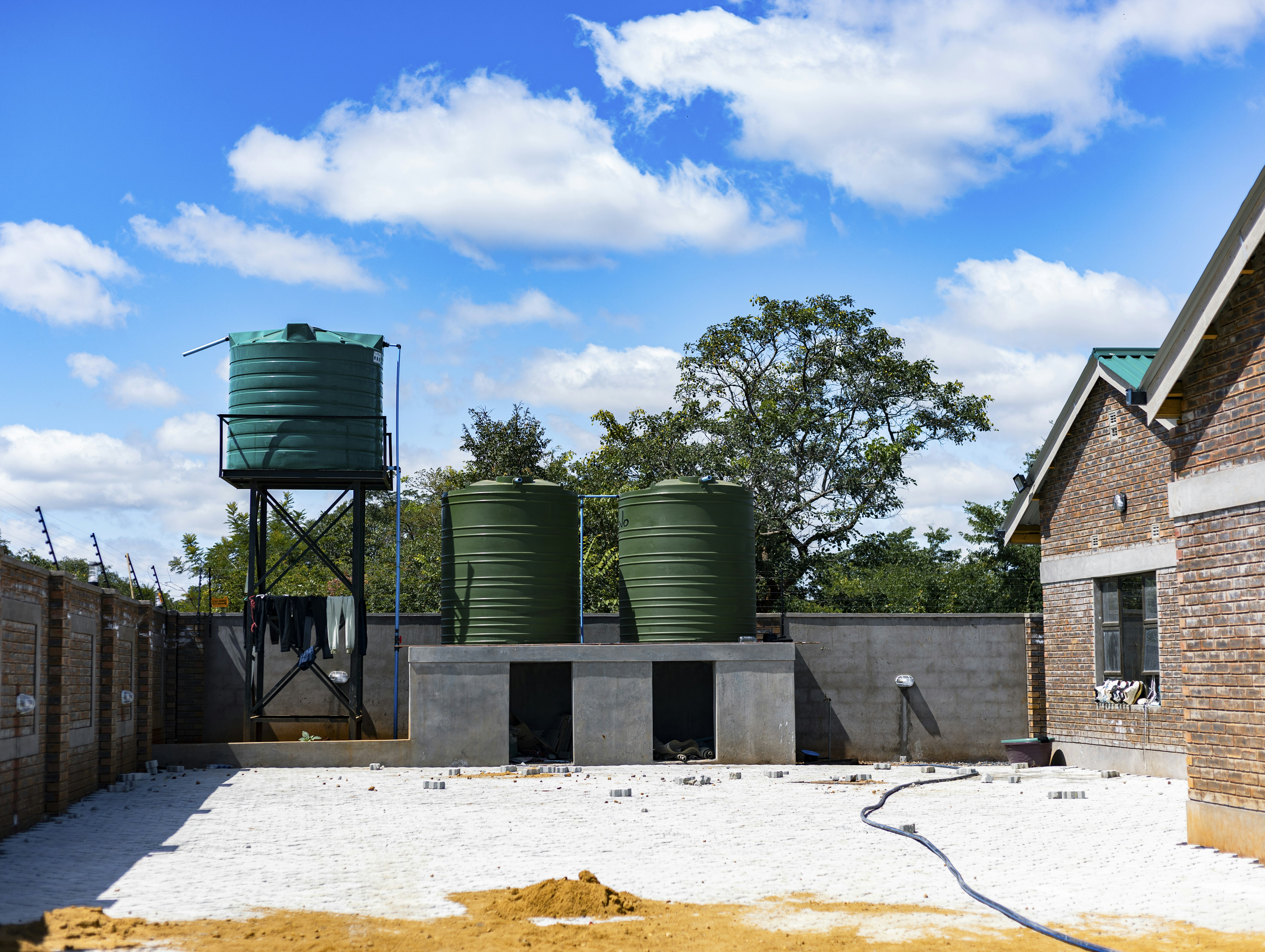 Three green plastic water tanks on a concrete platform in a brick courtyard