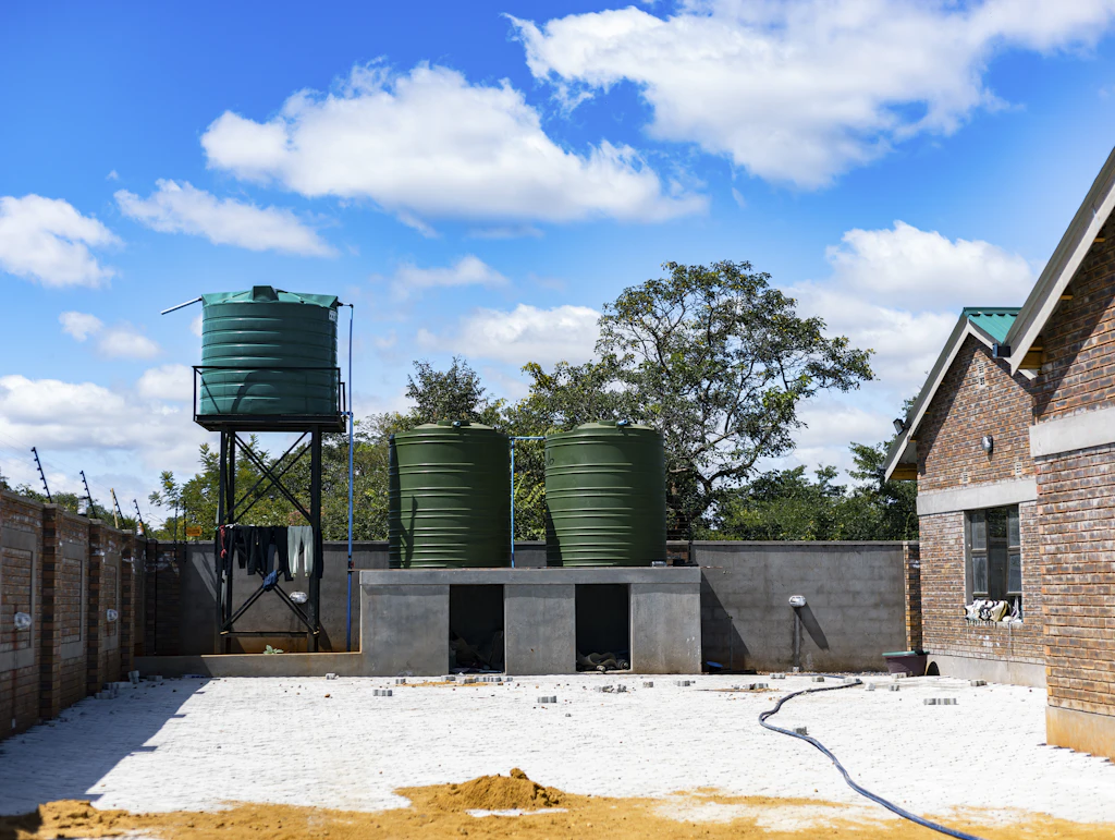 Three green plastic water storage tanks on a concrete stand, with a tall tank tower behind them