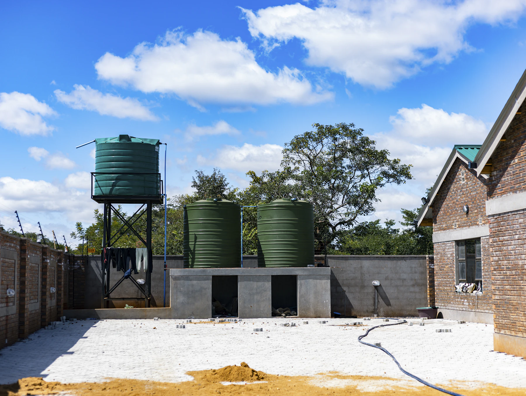 Three green plastic water tanks, one raised on a steel tower, in a paved brick courtyard