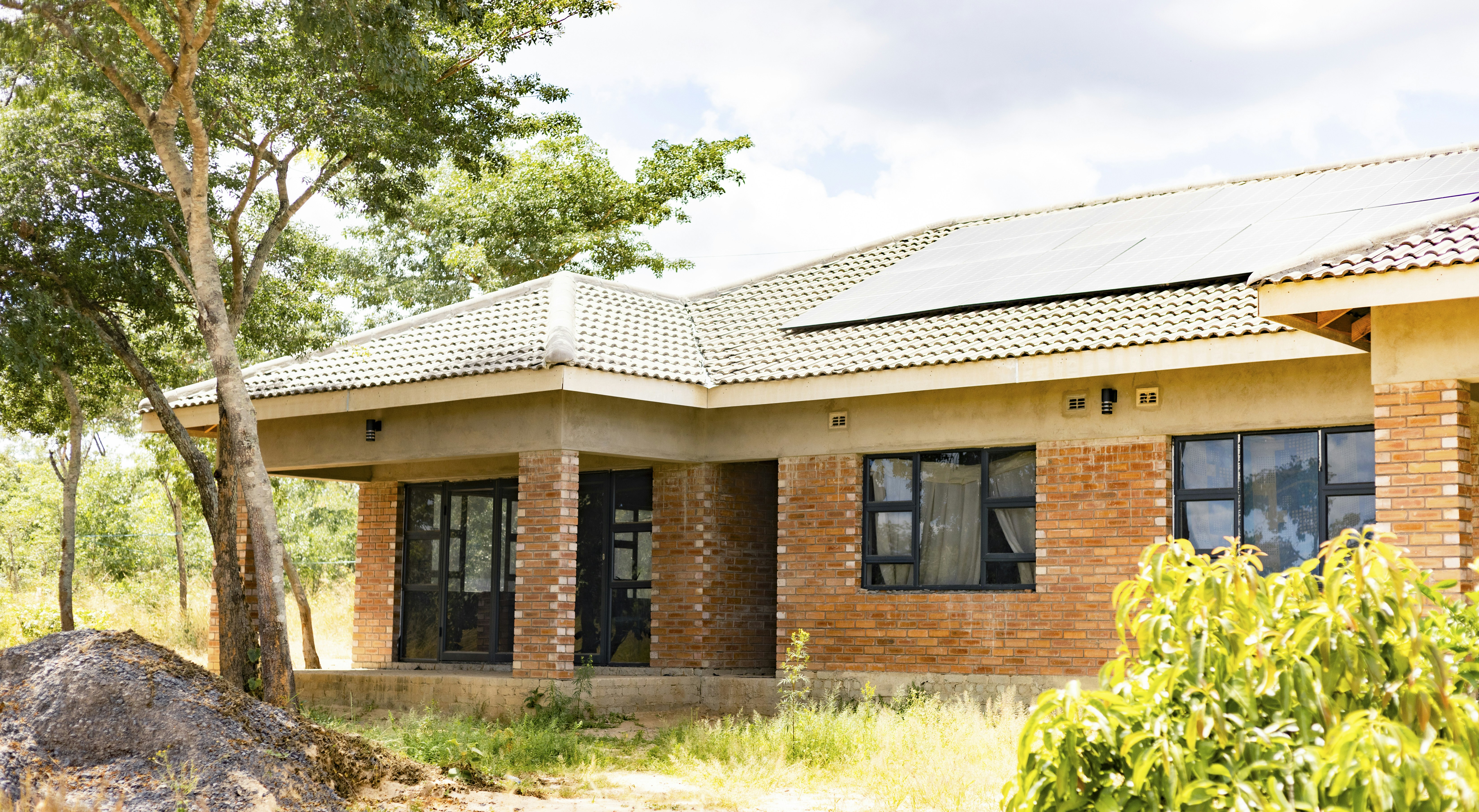 A single-story brick house with solar panels on a tiled roof in a rural setting