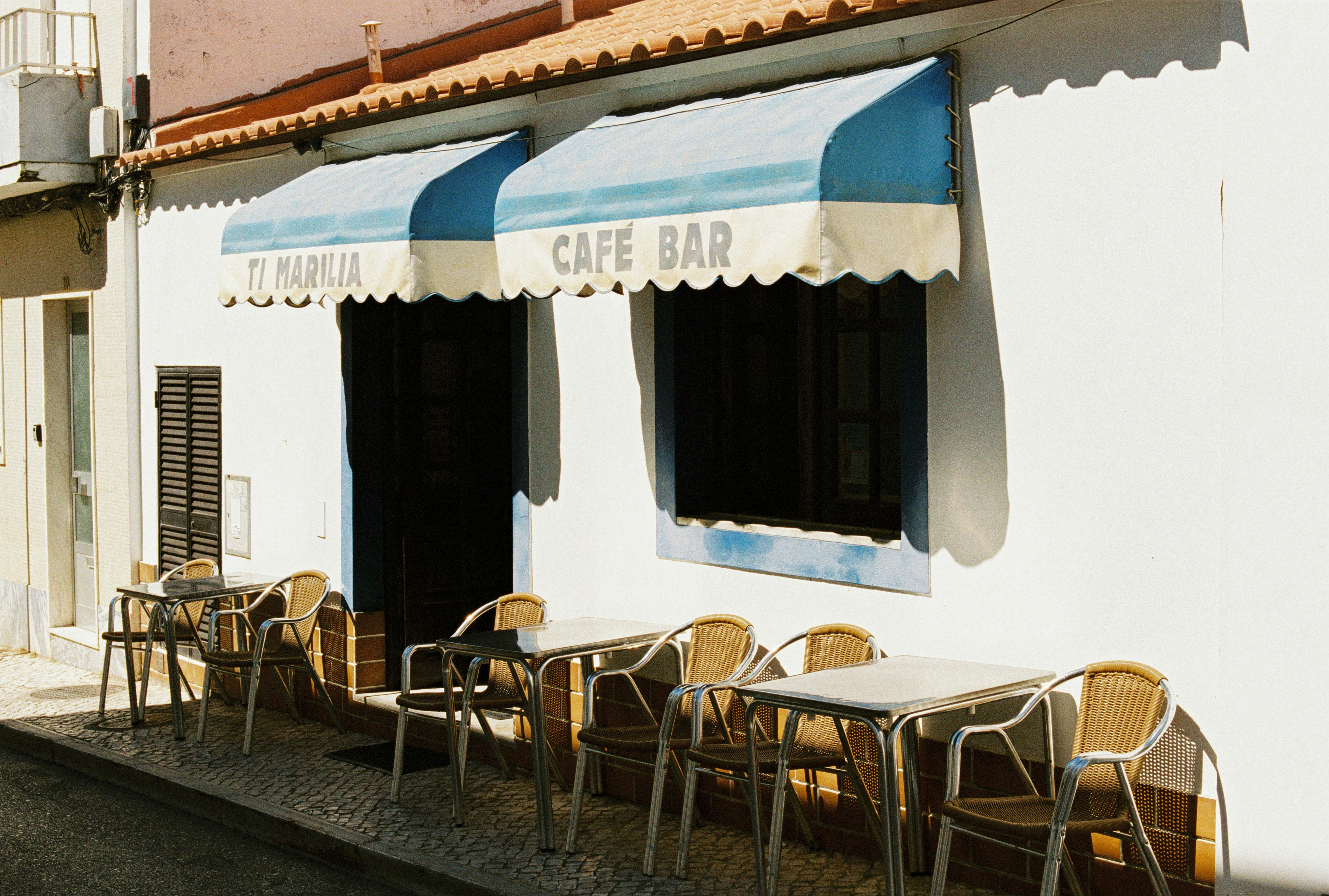 Rattan chairs and metal tables under blue-striped awnings at Ti Marilia cafe bar