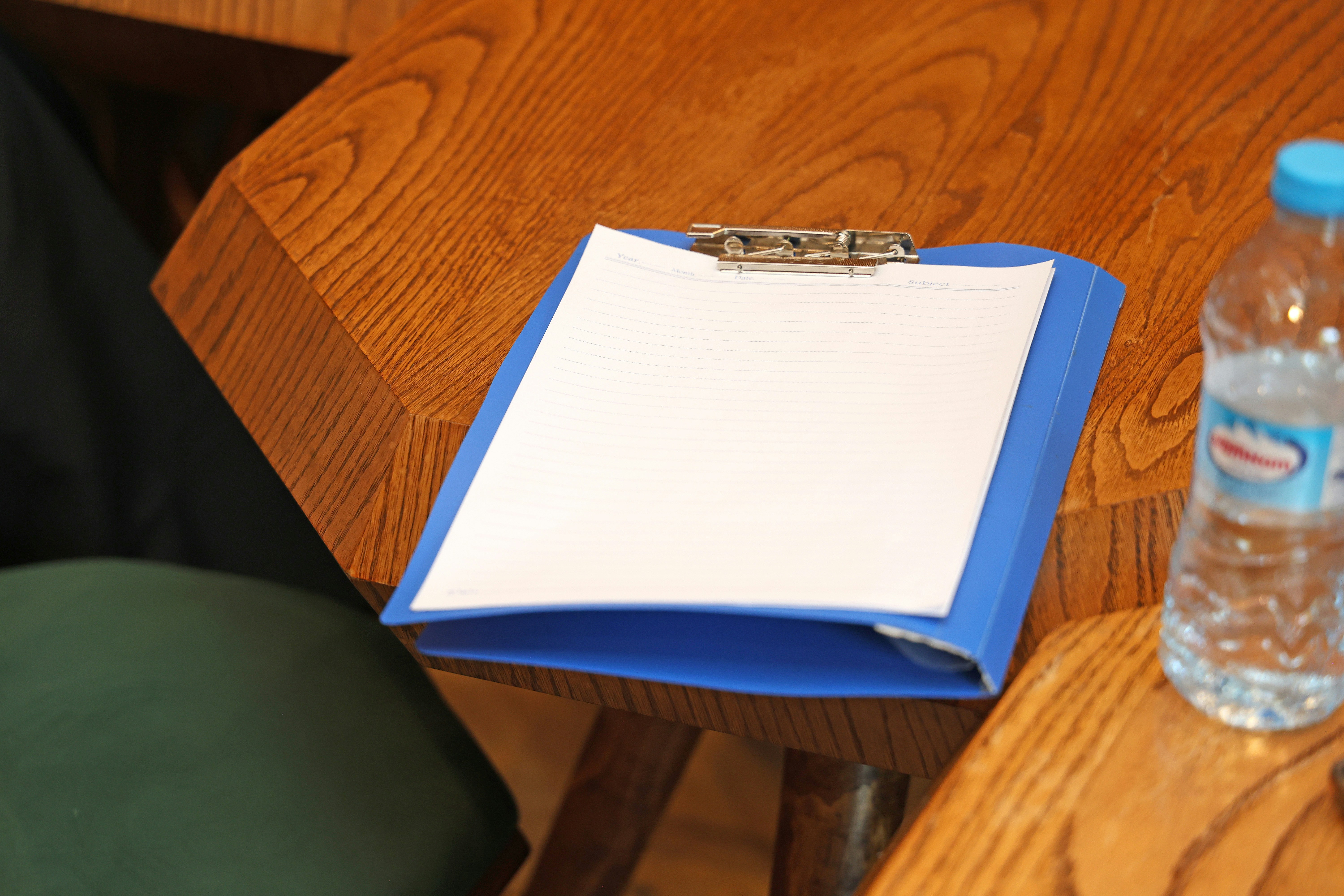 A blue clipboard with lined paper on a wooden table beside a water bottle